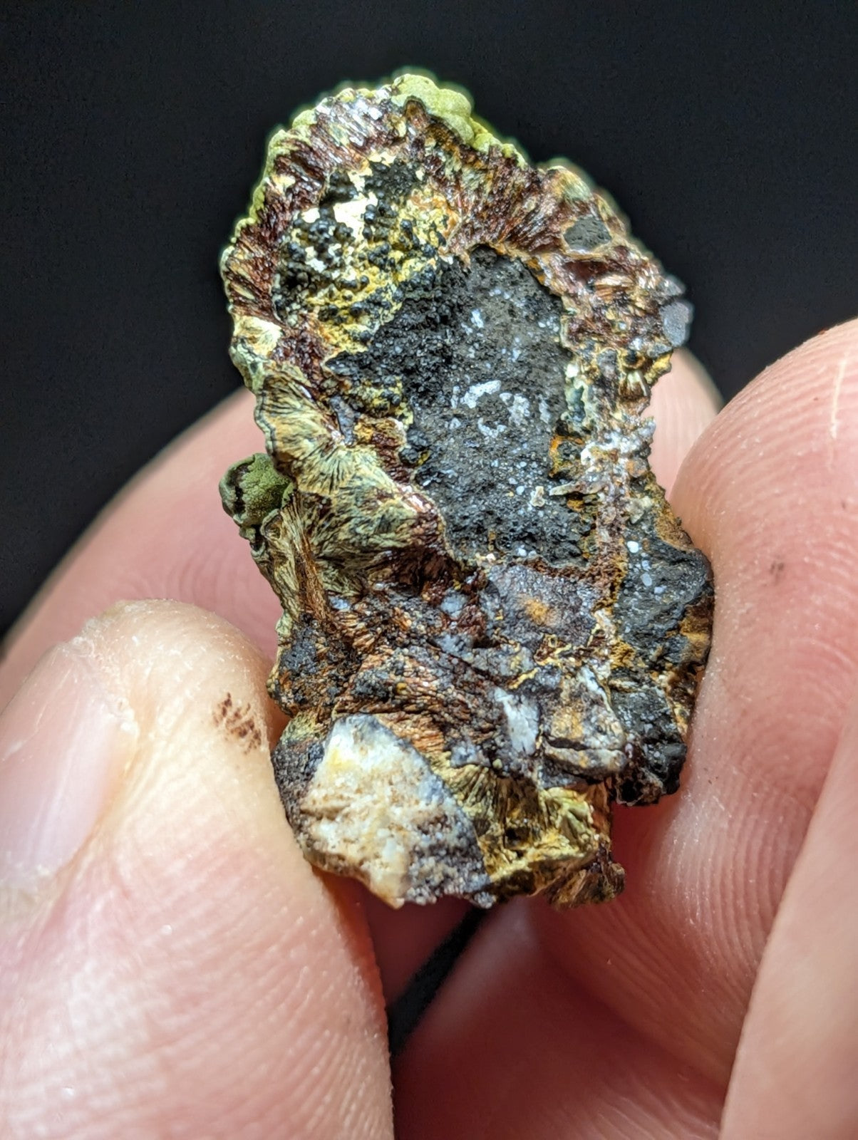 A rugged, irregularly shaped mineral specimen with a textured surface displaying patches of green, brown, black, and hints of yellowish hues.