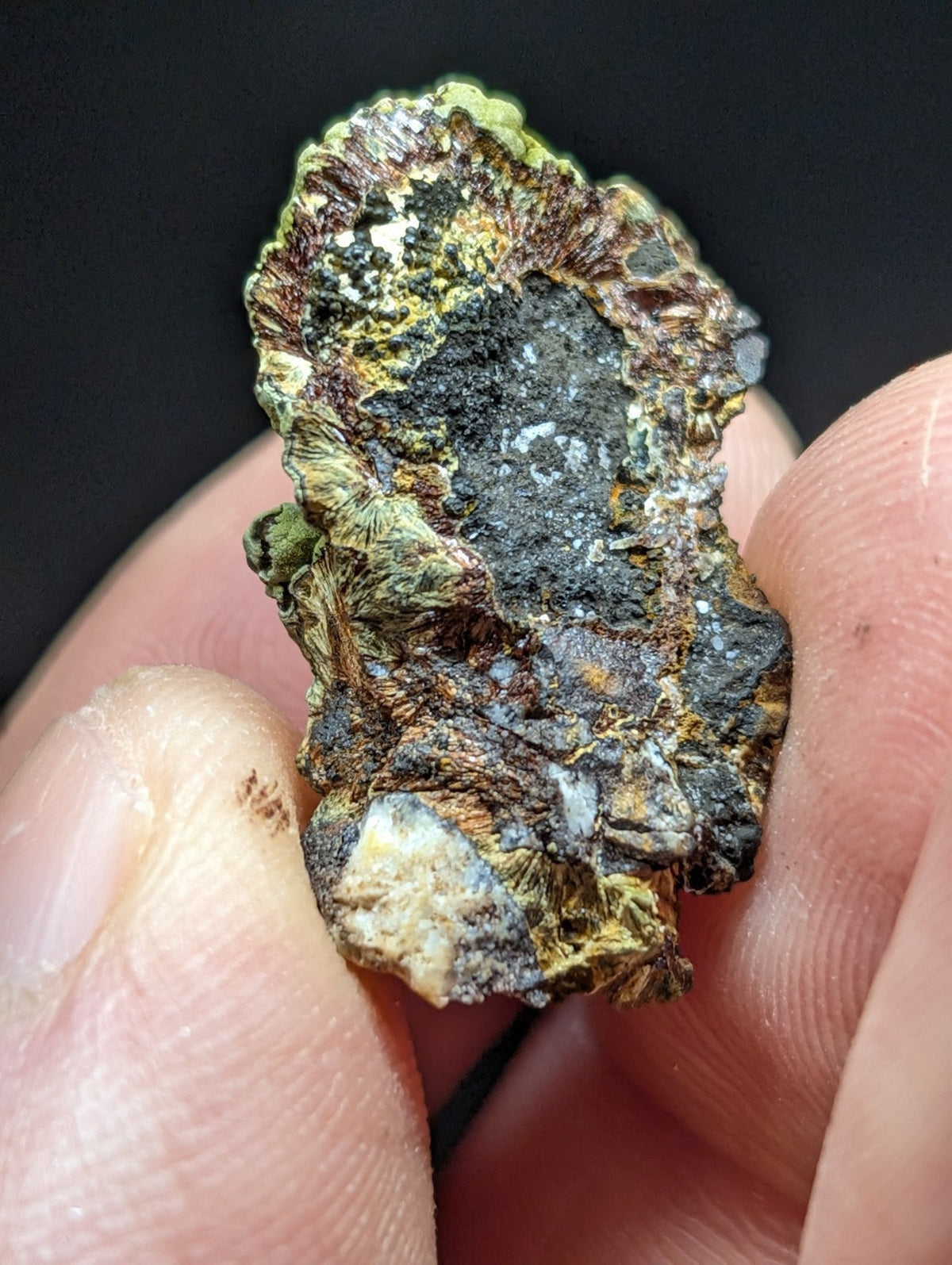 A rugged, irregularly shaped mineral specimen with a textured surface displaying patches of green, brown, black, and hints of yellowish hues.