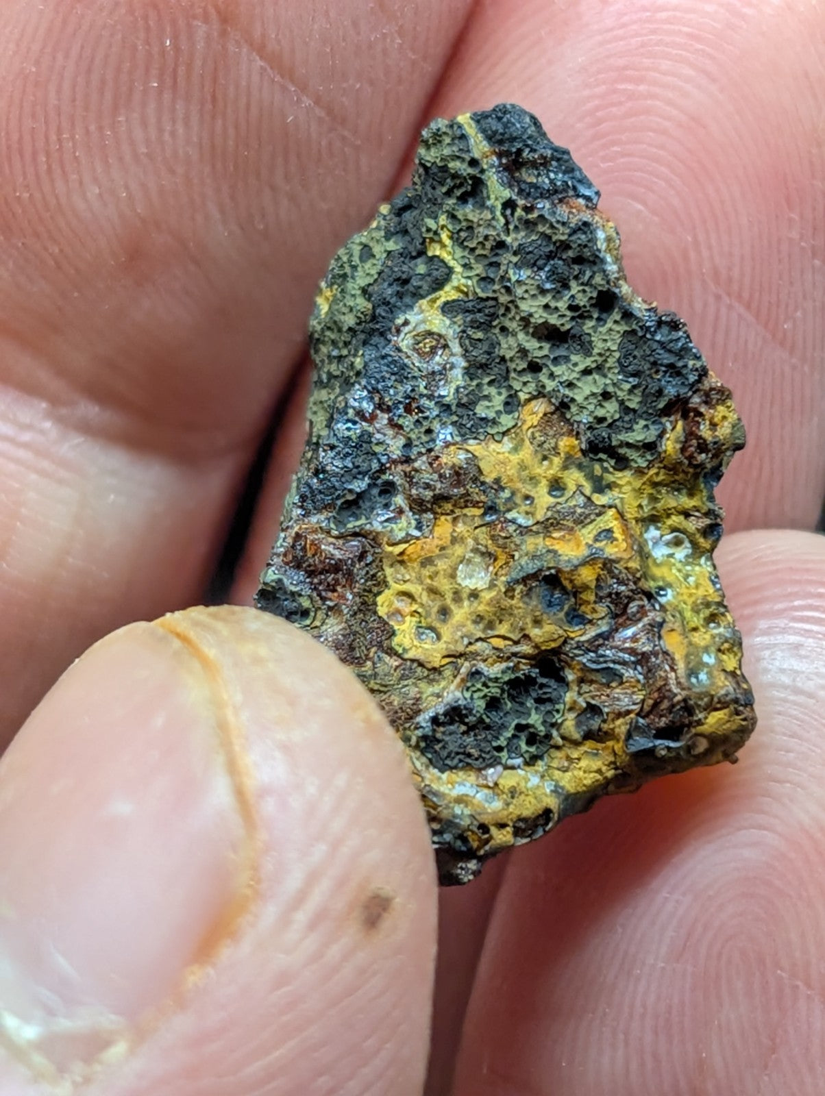 A rugged, irregularly shaped mineral specimen with a textured surface displaying patches of vibrant yellow and dark greenish-black hues.