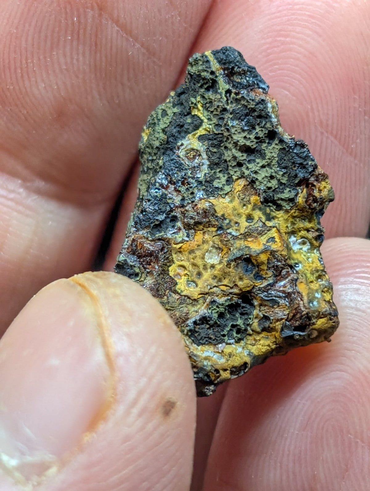 A rugged, irregularly shaped mineral specimen with a textured surface displaying patches of vibrant yellow and dark greenish-black hues.