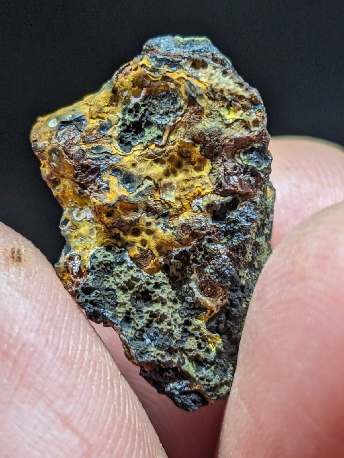 A rugged, irregularly shaped mineral specimen with a textured surface displaying patches of vibrant yellow, deep green, and dark brown.