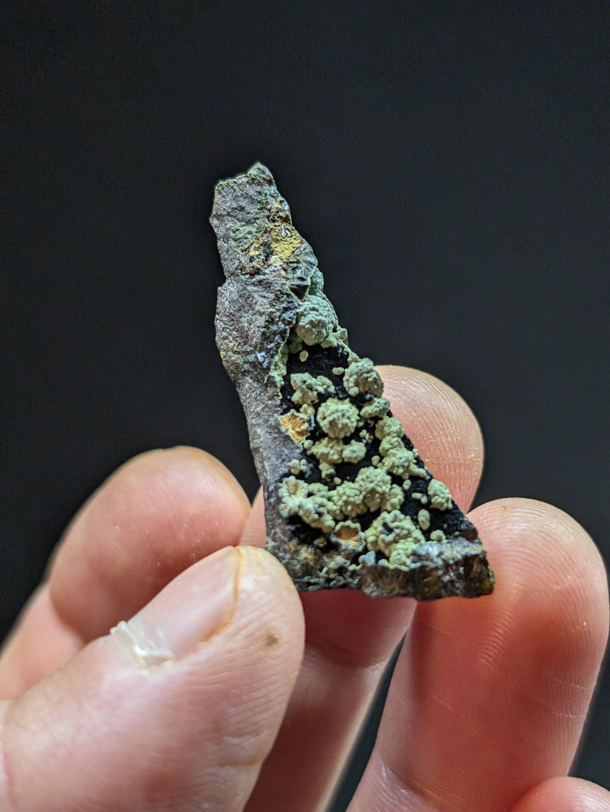 A weathered, irregularly shaped mineral specimen with a dark gray base and patches of greenish-blue lichen-like growths.