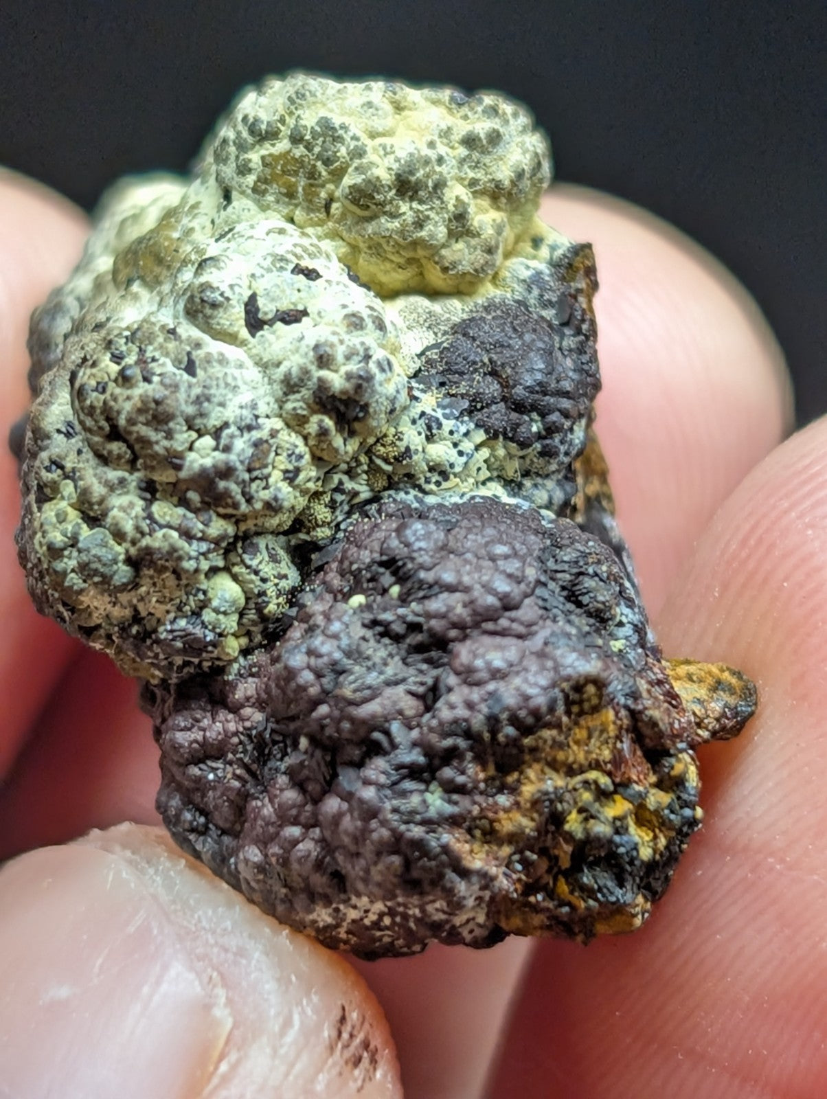 A rugged, irregularly shaped mineral specimen with a textured surface featuring patches of greenish-yellow and dark brown to black hues.