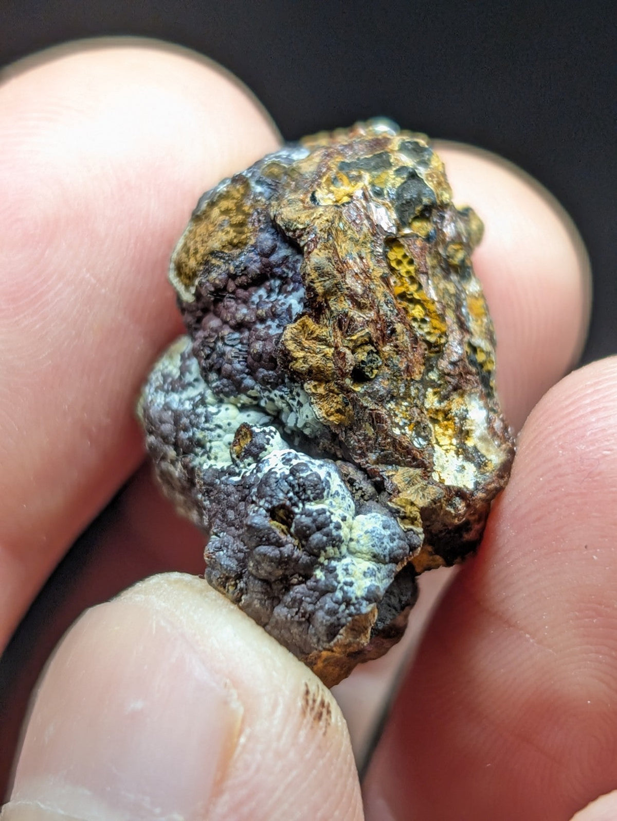 A rugged, multi-colored mineral specimen with patches of yellow, dark gray, and greenish-blue patina.