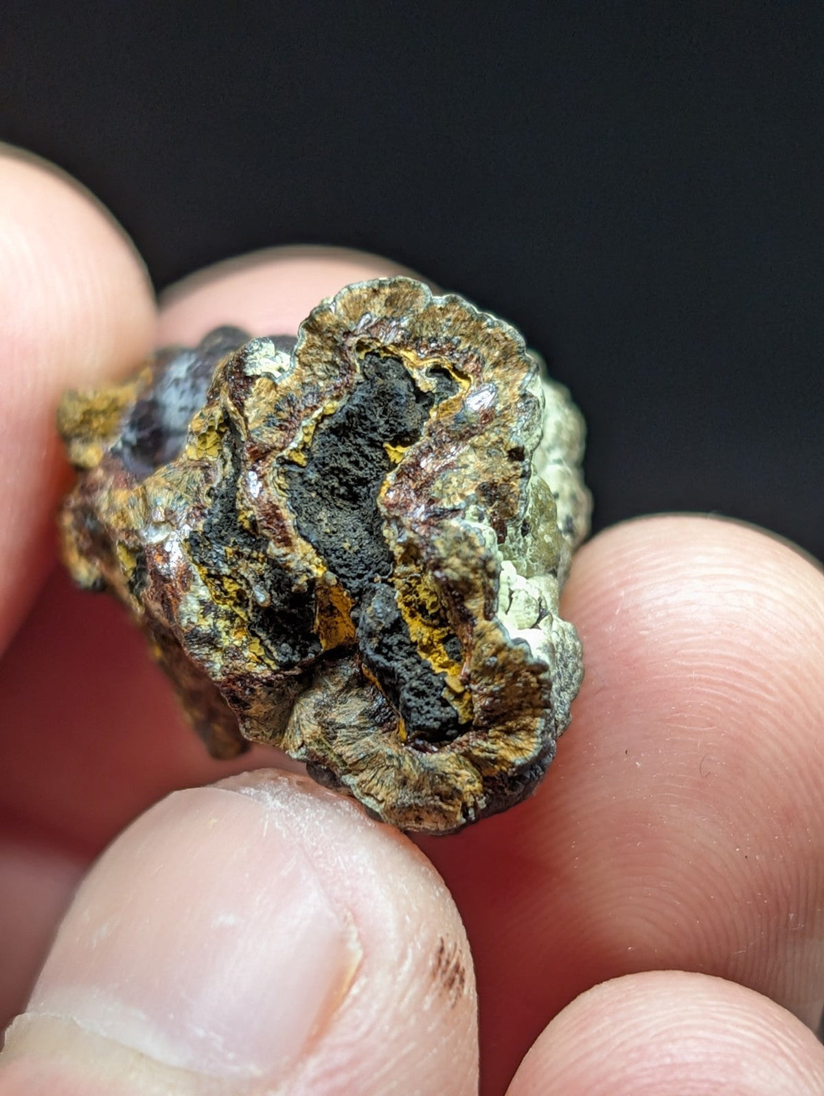A rugged, irregularly shaped mineral specimen with a mottled surface of dark gray, black, and earthy yellowish-brown hues.