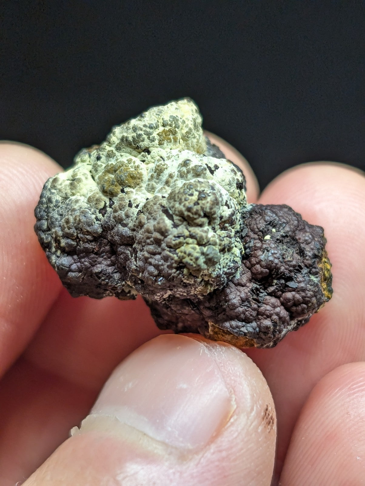 A rough, irregularly shaped mineral specimen with a textured surface displaying patches of dark gray and greenish hues.