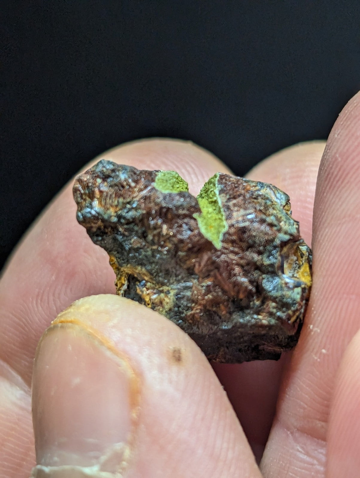 A rugged, irregularly shaped mineral specimen with a dark brown base and patches of vibrant green patina.