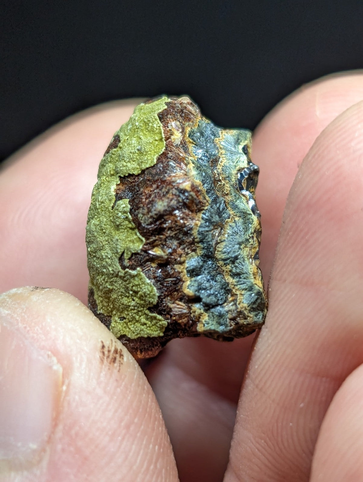 A rugged, irregularly shaped mineral specimen with patches of vibrant green moss-like growth over a textured surface displaying earthy brown and bluish-gray tones.