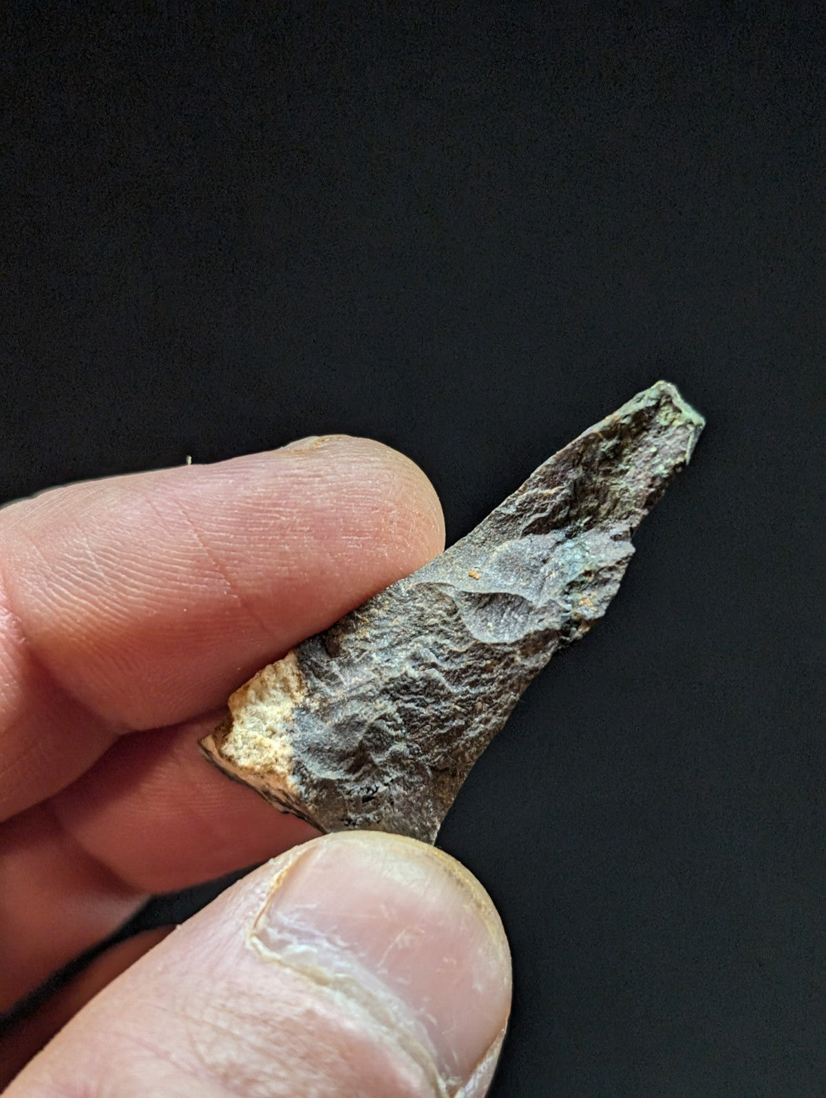 A weathered, dark gray stone flake with a rough texture and subtle greenish patina.