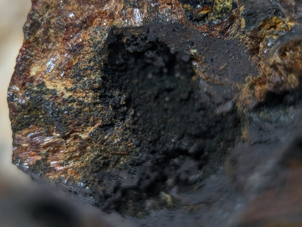 A rugged, dark metallic rock with patches of rust-colored and greenish mineral deposits.