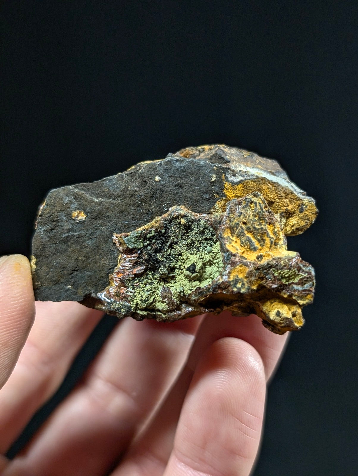 A rugged, irregularly shaped rock with a dark gray base and vibrant patches of green and yellow mineral growth.