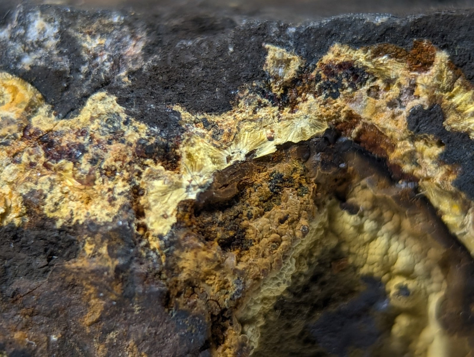 A rugged, textured mineral specimen with patches of vibrant yellow and orange oxidation contrasting against dark, weathered rock.
