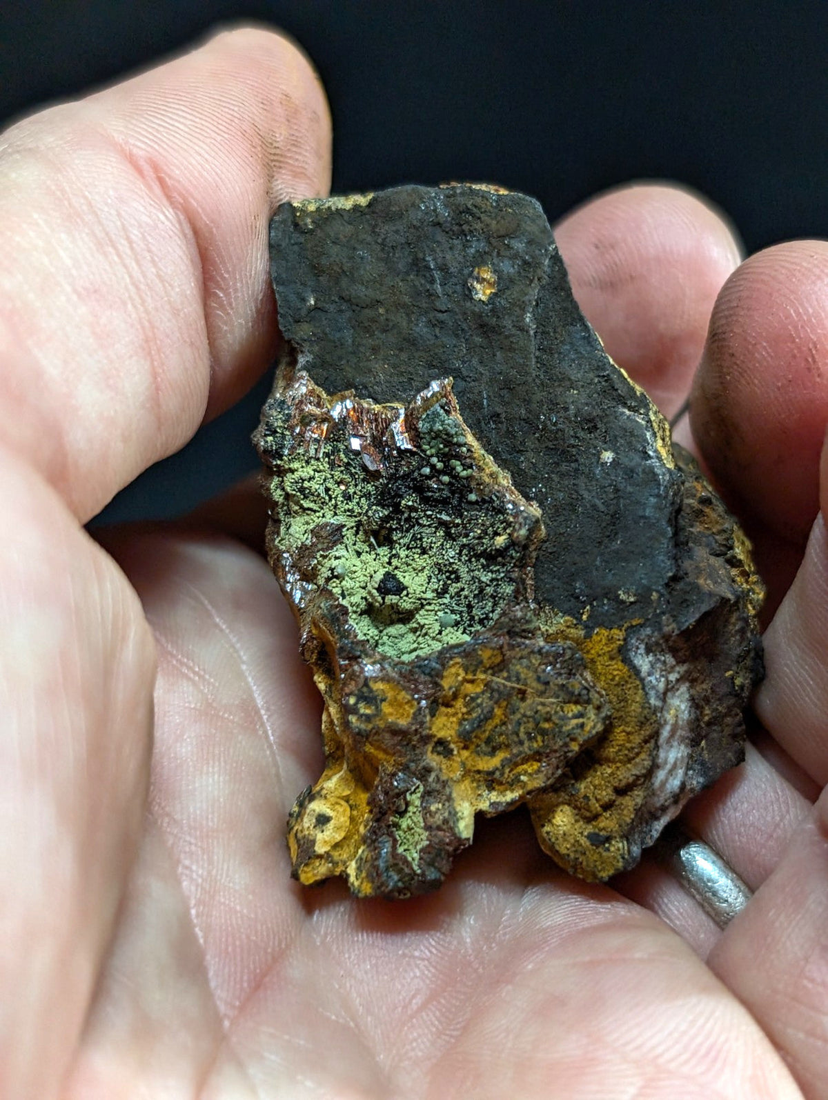 A rugged, irregularly shaped rock with a dark base and patches of vibrant green and yellow mineral growth.