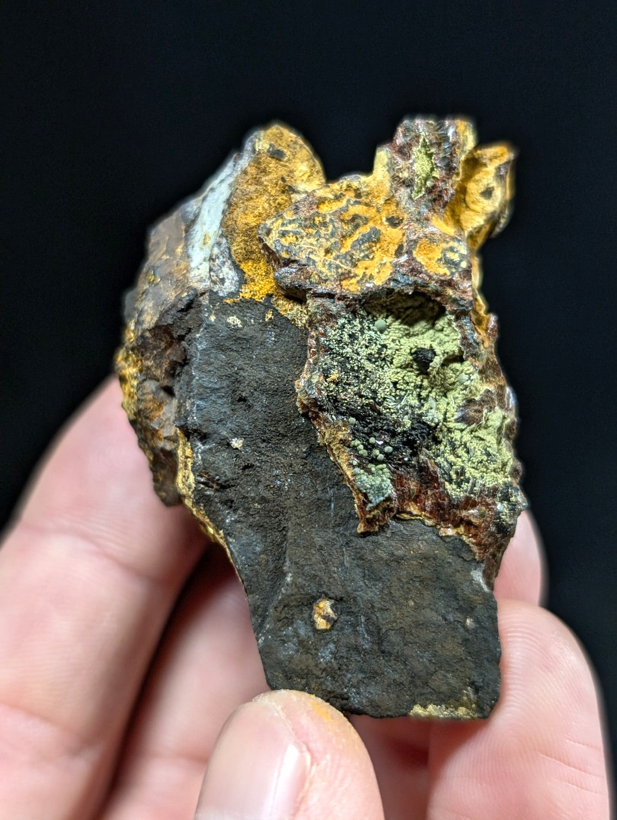 A rugged, irregularly shaped rock with a dark base and patches of vibrant yellow-orange rust-like mineral formations alongside areas of greenish patina.