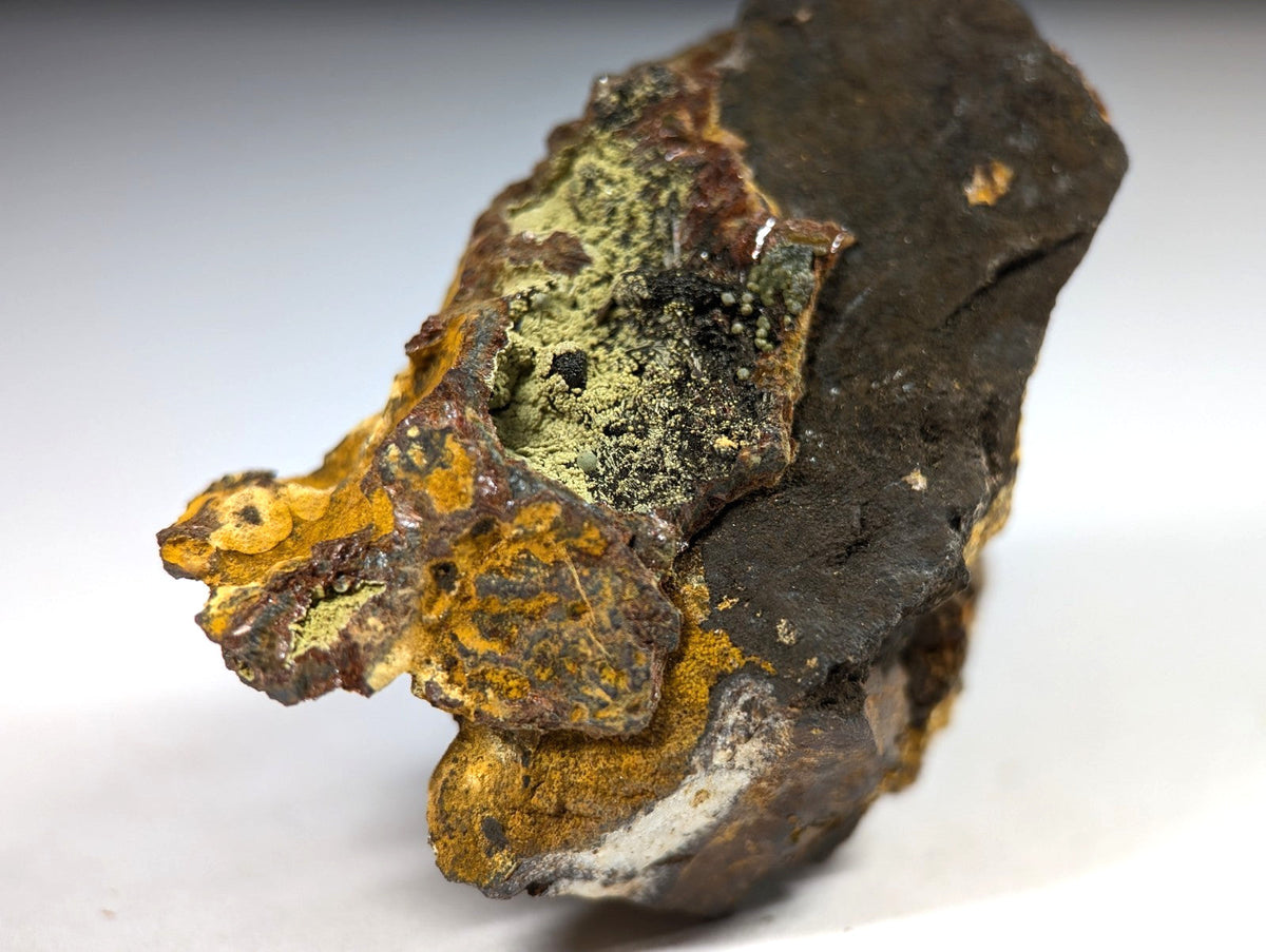 A rugged, irregularly shaped rock specimen featuring patches of vibrant yellow and green mineral deposits against a dark brown base.