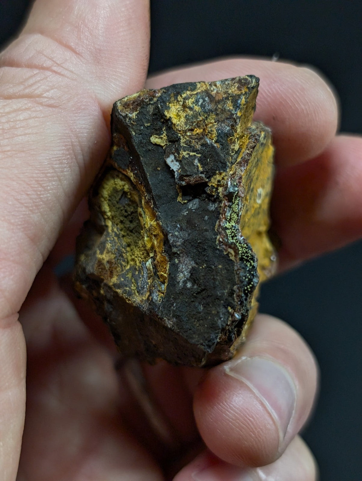 A rugged, irregularly shaped mineral specimen with a dark base and vibrant yellow-orange patches of oxidation.