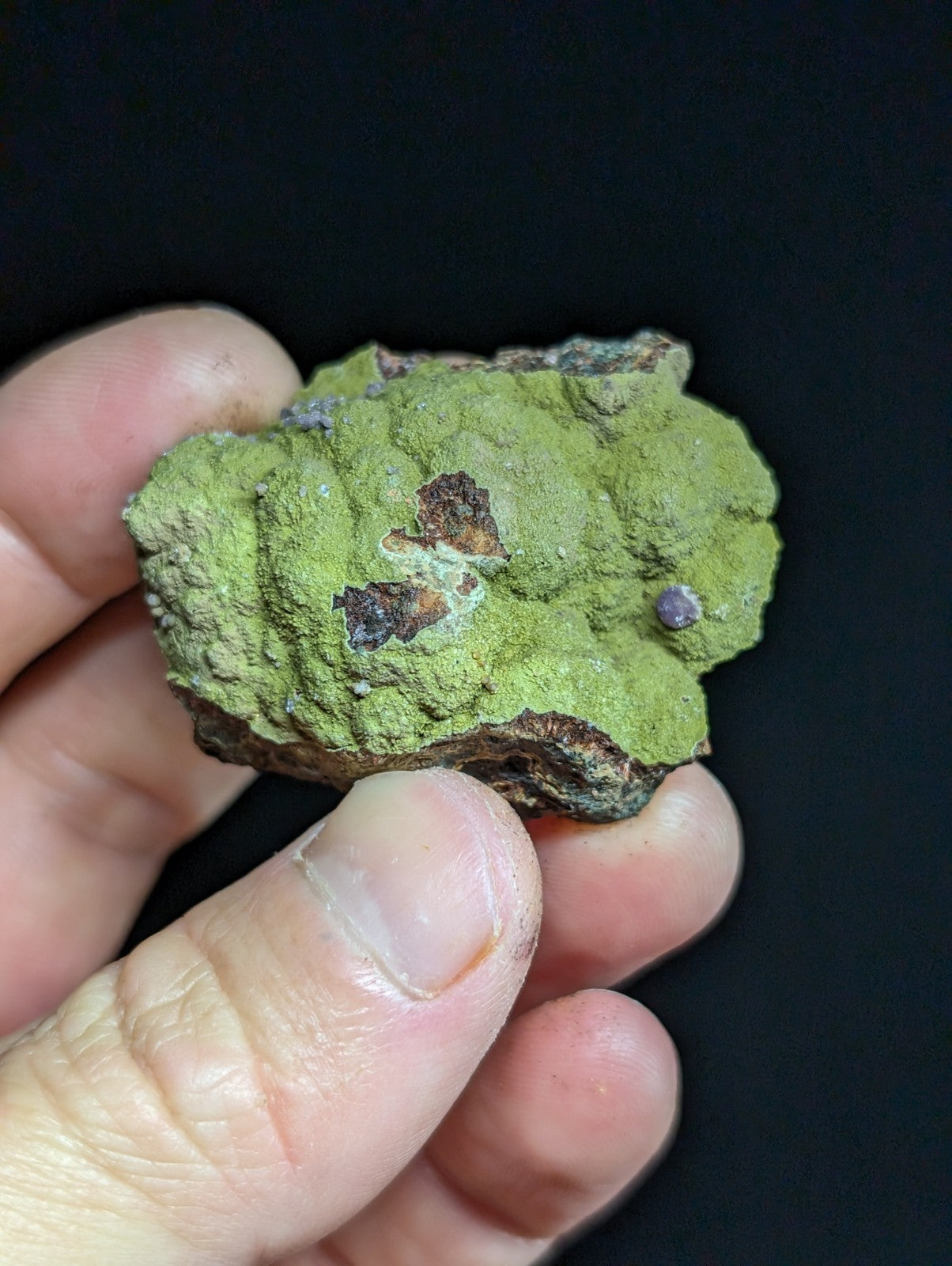 A rough, irregularly shaped mineral specimen with a vibrant green surface and patches of brownish discoloration.