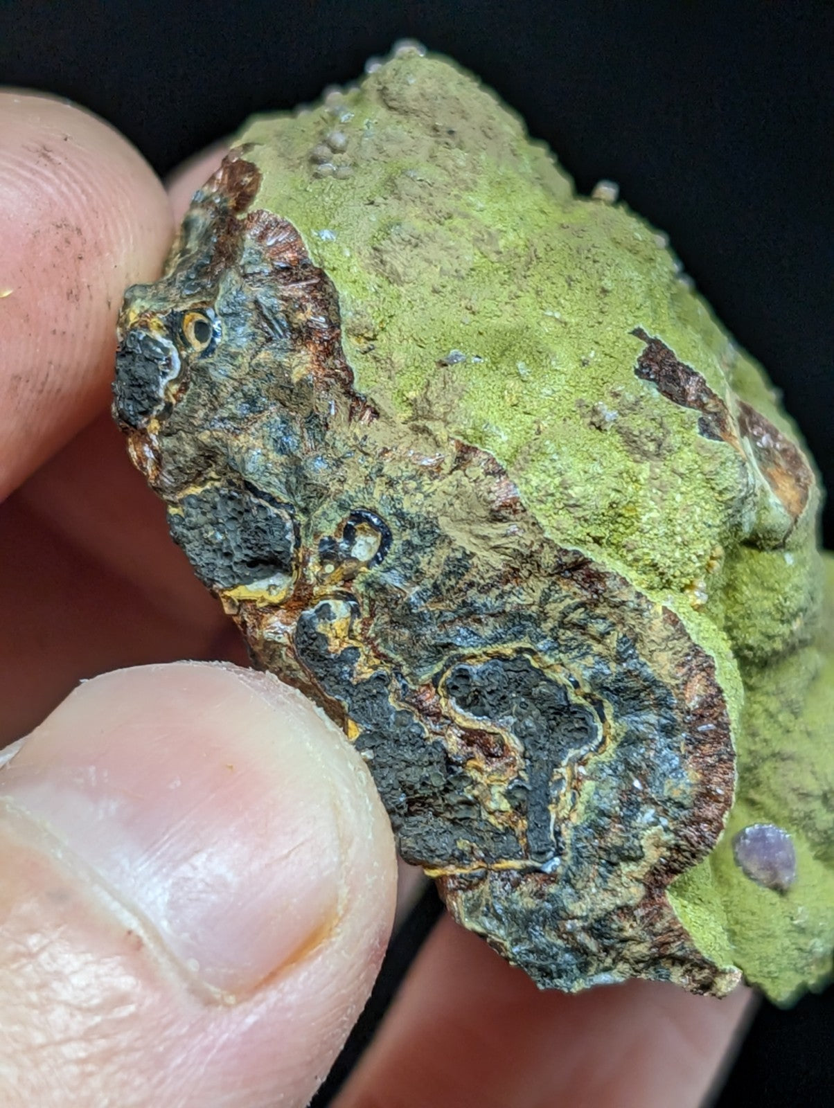 A rough, irregularly shaped mineral specimen with a vibrant green mossy coating over dark, textured rock.