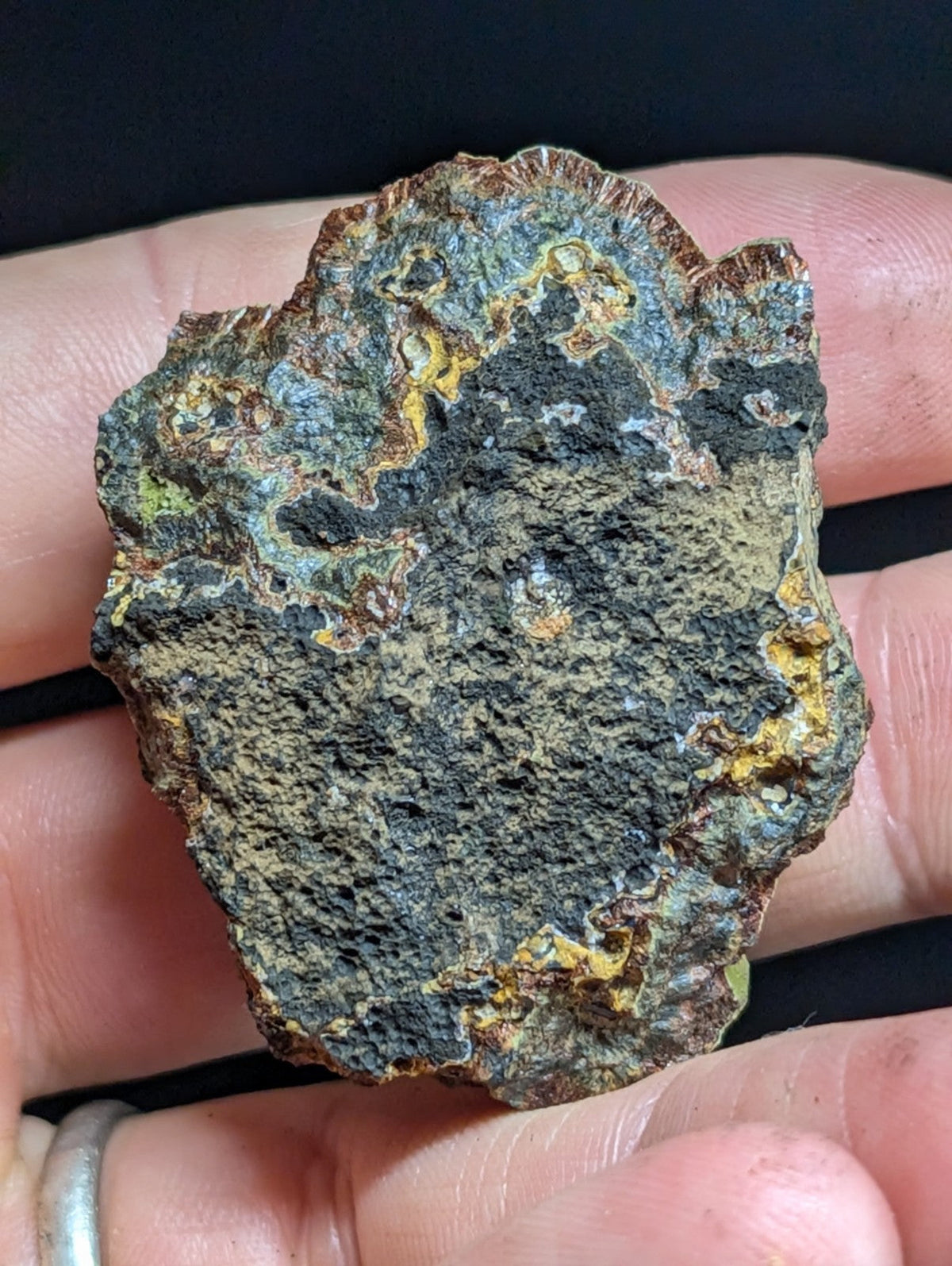 A rugged, irregularly shaped meteorite with a dark gray surface streaked with patches of greenish-blue and yellow rust-like patina.