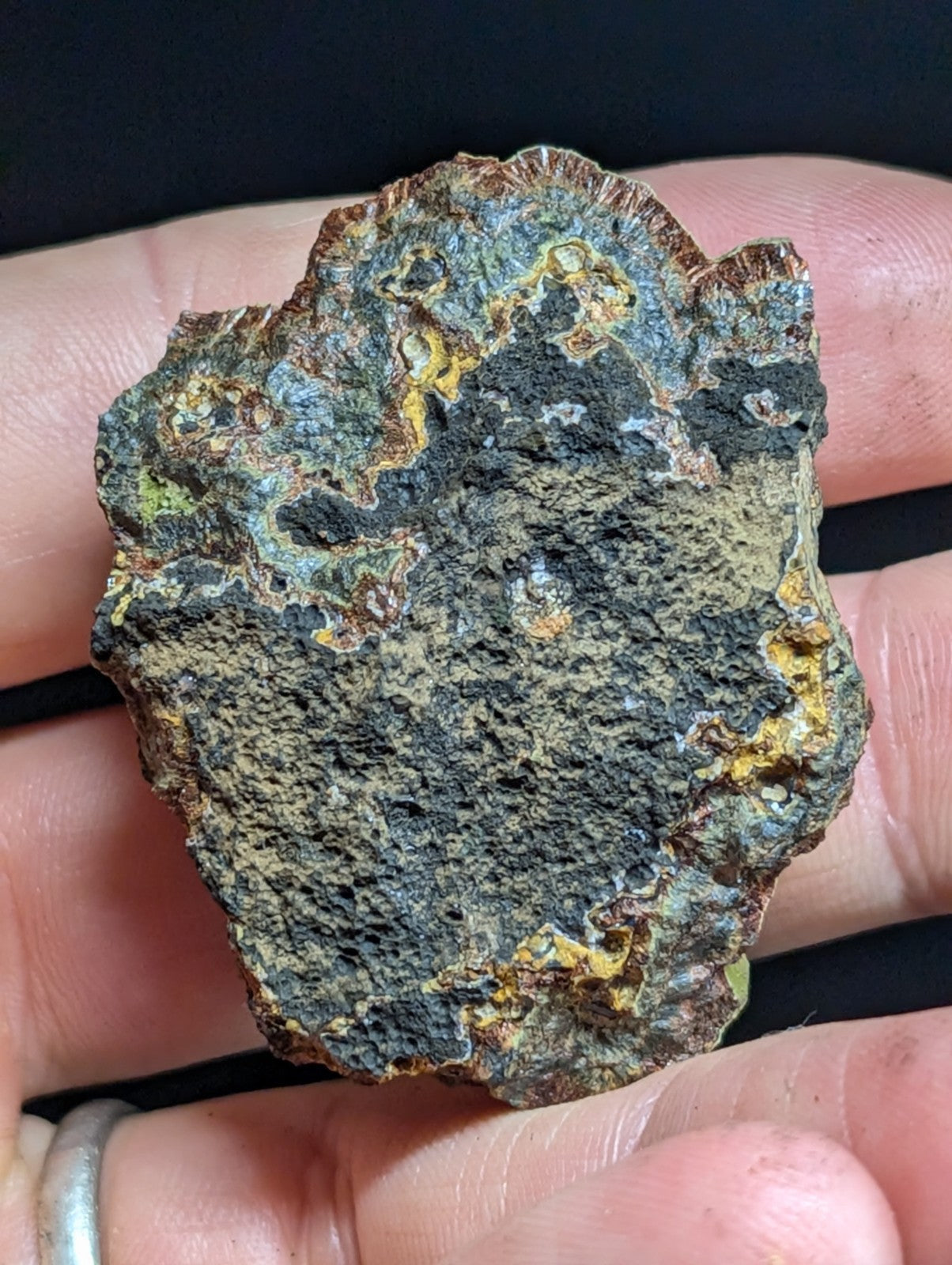 A rugged, irregularly shaped meteorite with a dark gray surface streaked with patches of greenish-blue and yellow rust-like patina.