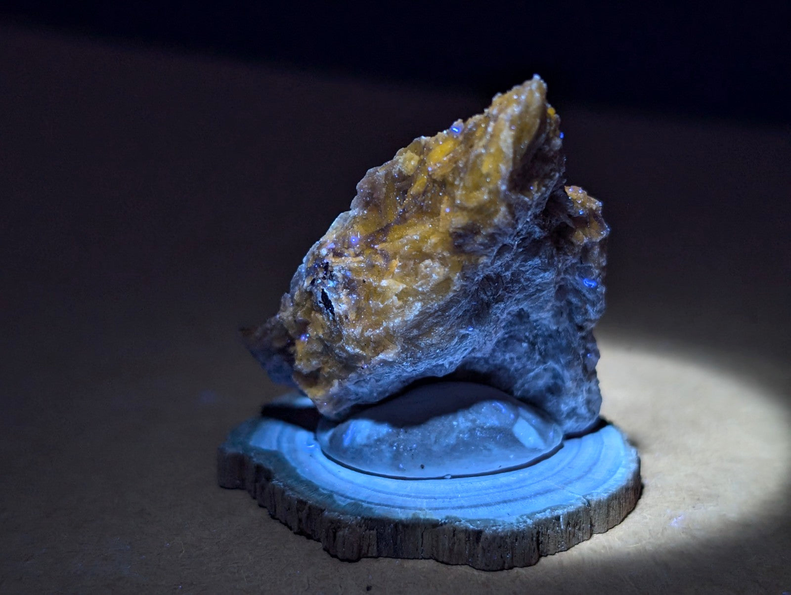 A striking yellow and blue mineral specimen with crystalline textures, displayed on a rustic wooden slice base.