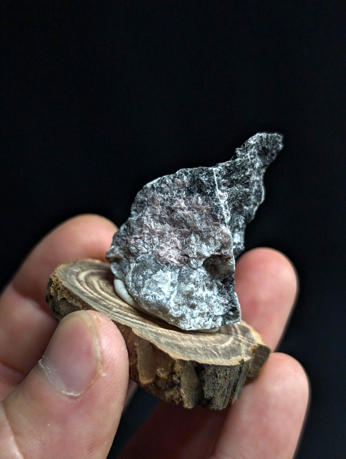 A rough, irregularly shaped gray stone with subtle pink and white veining rests on a small circular wooden slice.