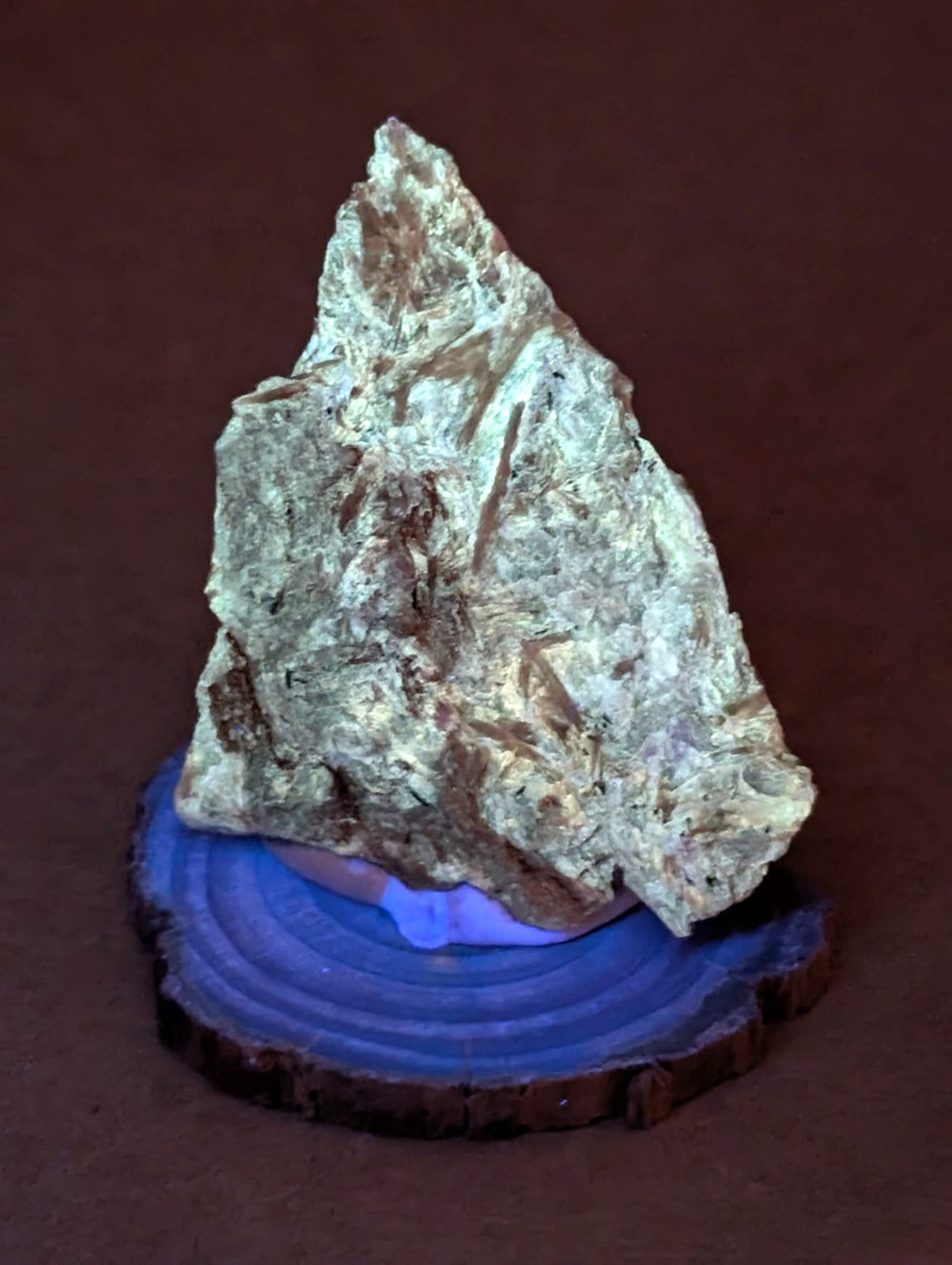 A rugged, light green and brown mineral specimen with a rough, textured surface sits atop a circular wooden base.