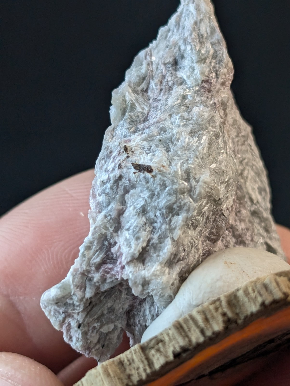 A textured, grayish-white mineral specimen with subtle purple undertones and a rough, crystalline surface.