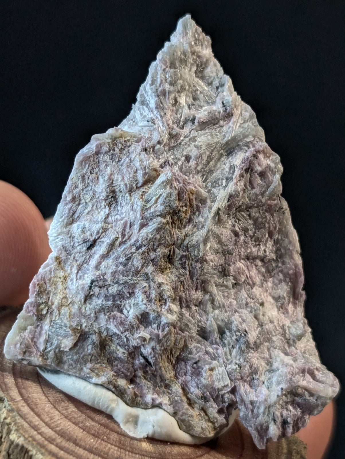A rough, triangular-shaped mineral specimen with a textured surface displaying shades of gray and purple.