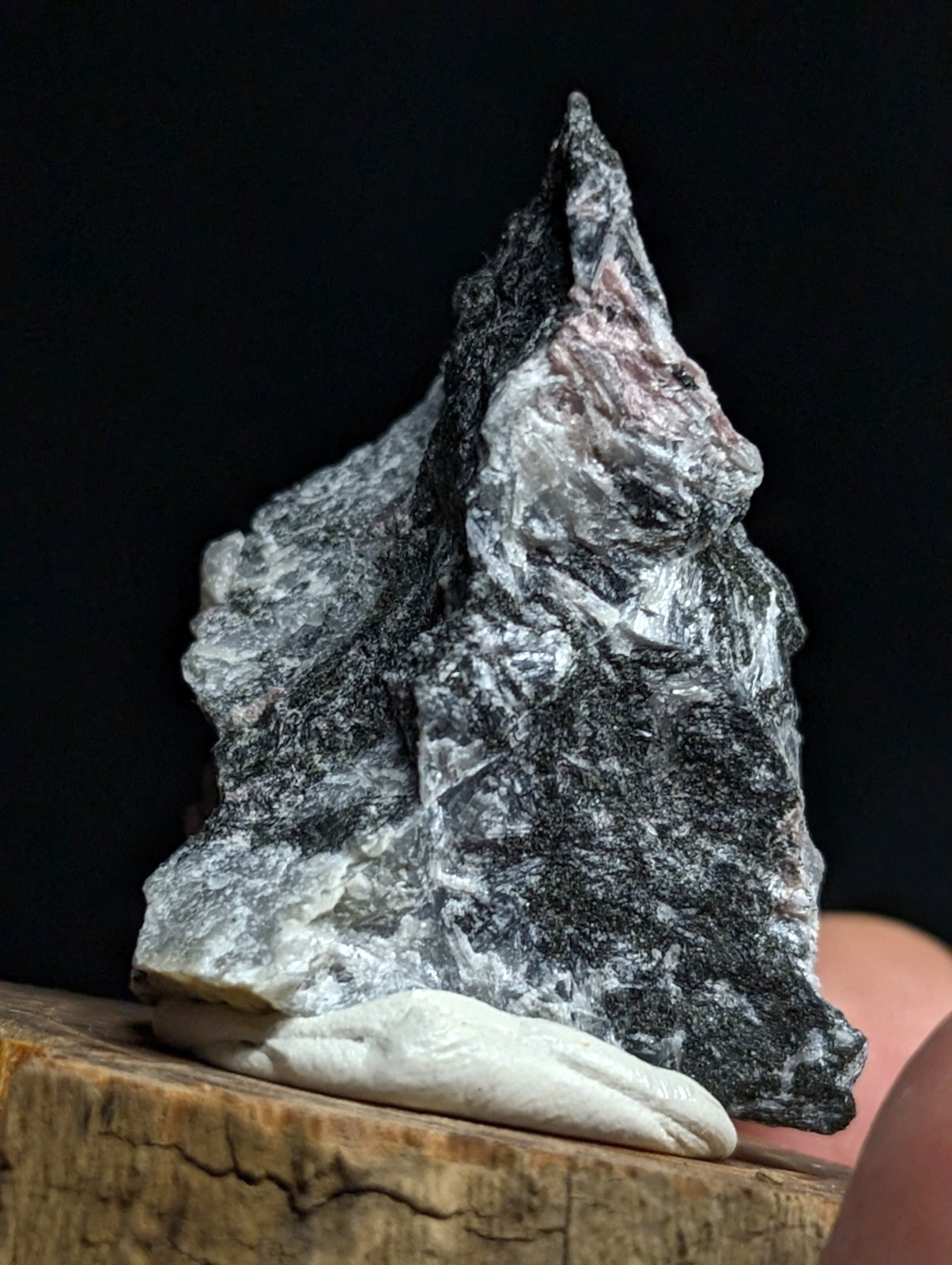 A striking black and white mineral specimen with a rough, jagged surface and subtle pinkish hues near its peak.
