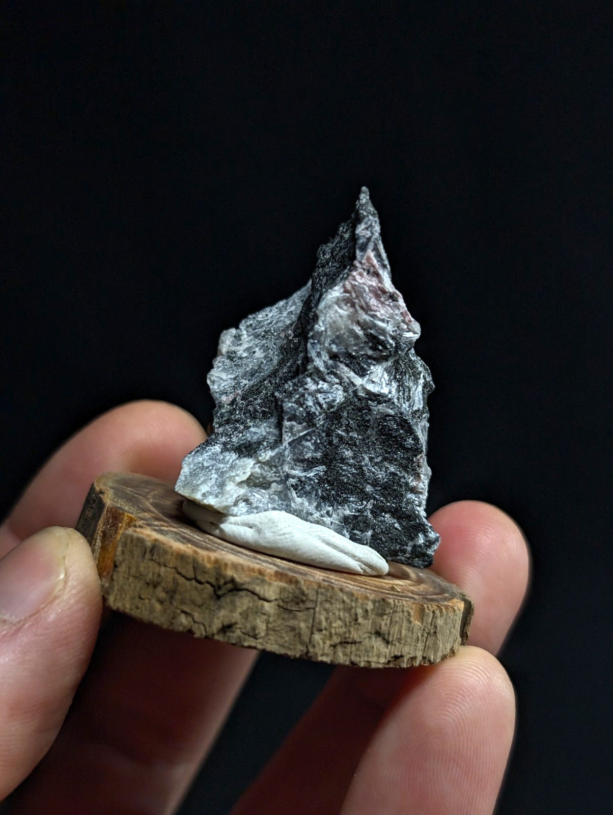 A dark gray, jagged rock specimen with subtle pinkish hues rests on a circular wooden slice.