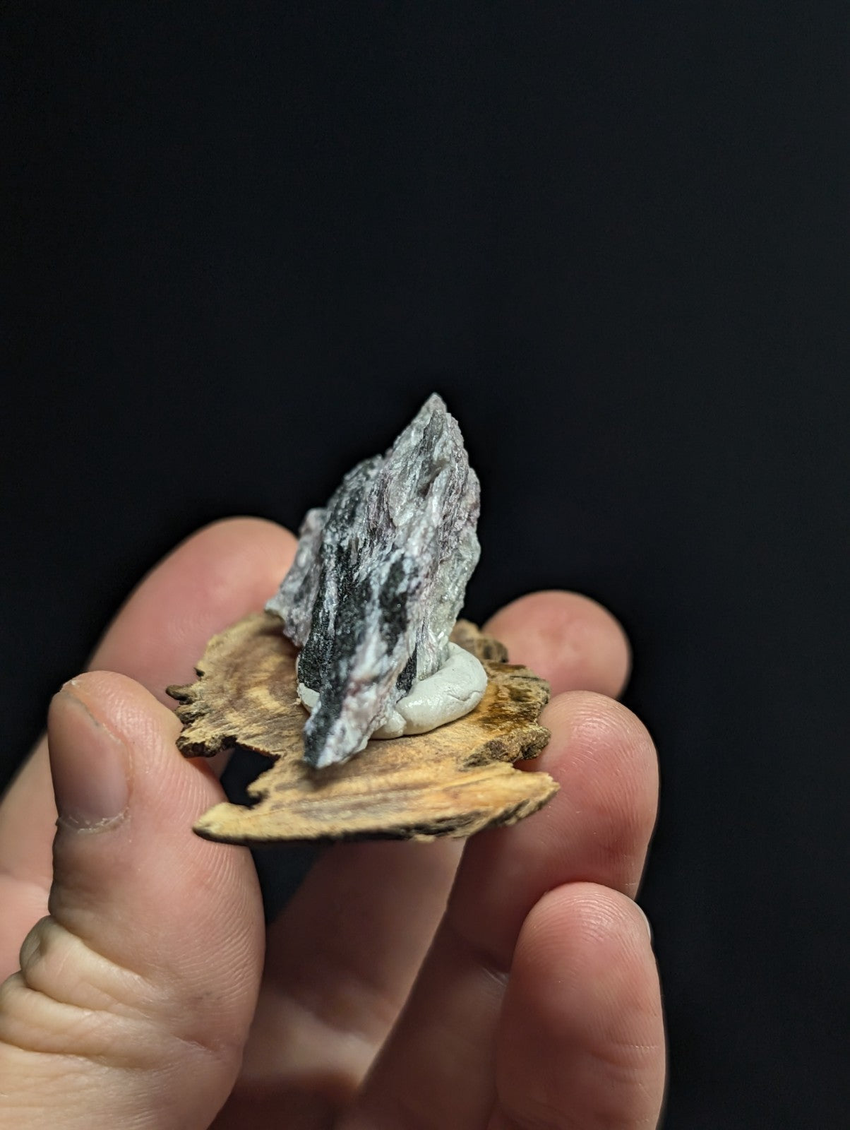 A gray, textured mineral specimen with a rough, jagged surface rests on a natural wood base.