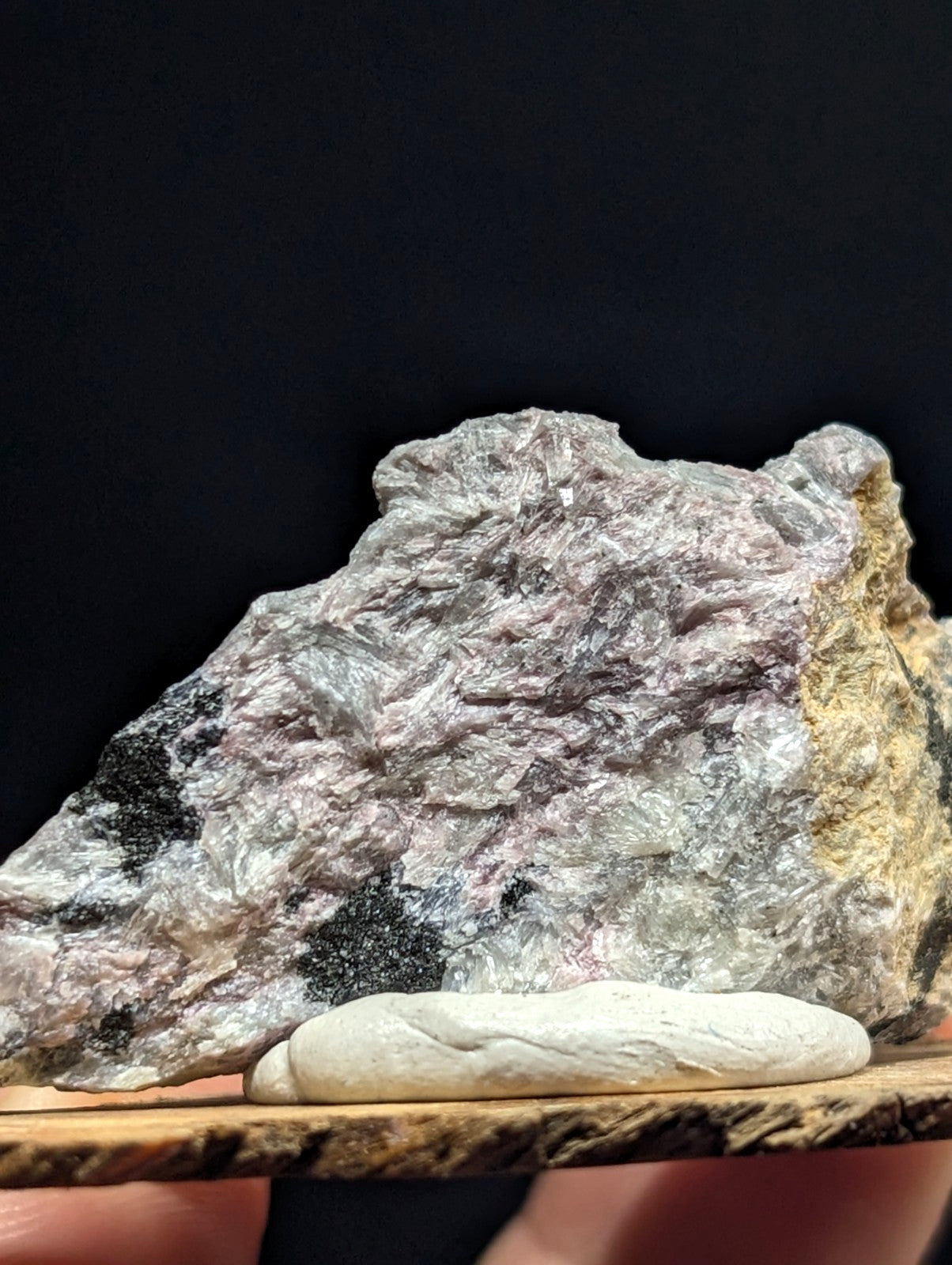 A rugged, naturally occurring mineral specimen with a mottled surface of gray, pinkish hues and dark inclusions.