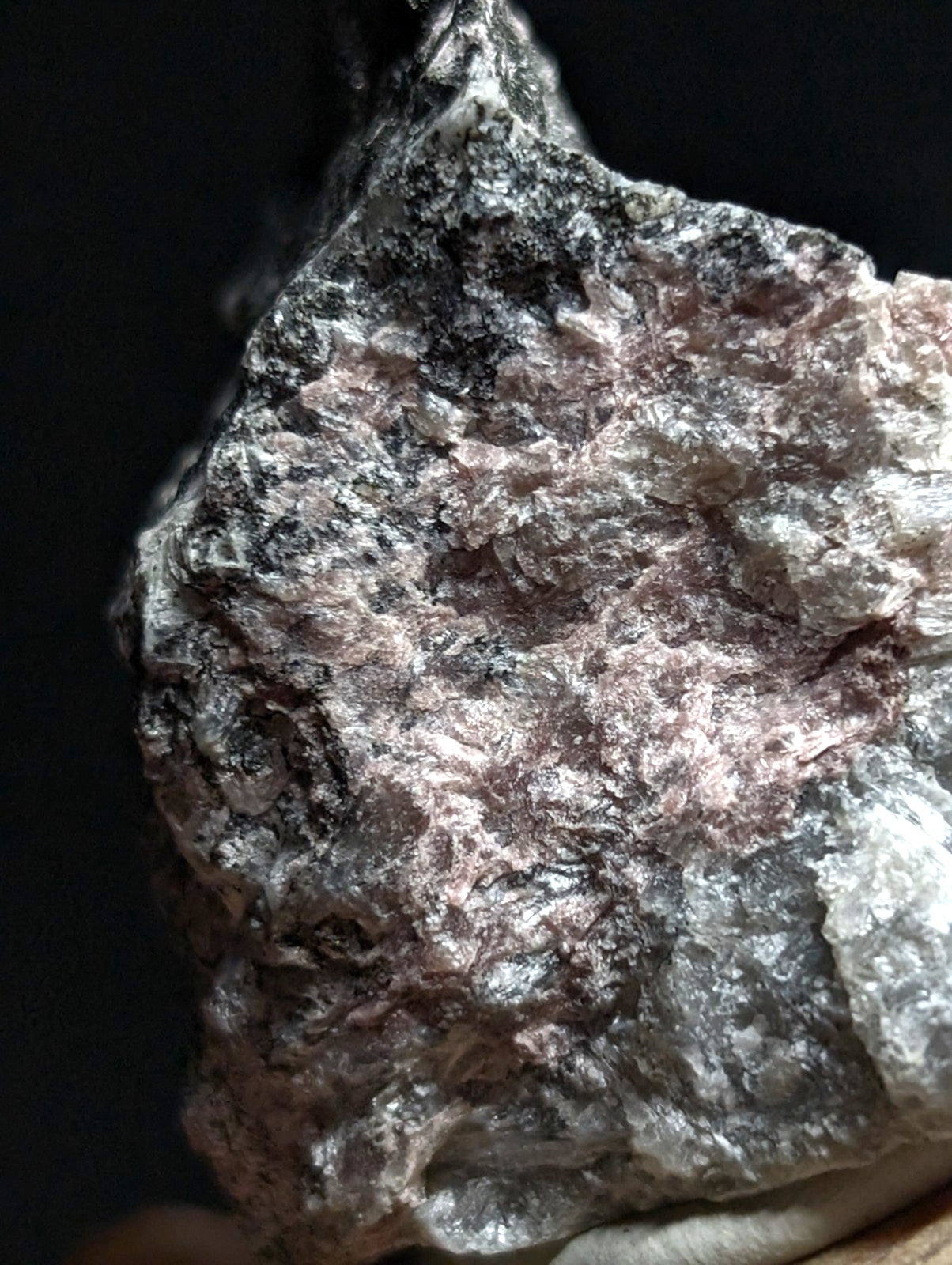 A rough, irregularly shaped mineral specimen with a mottled surface of pinkish-gray and dark patches.