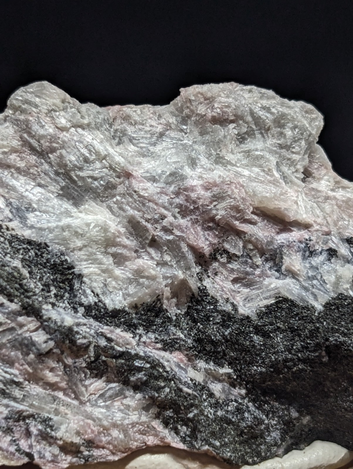 A rugged, naturally occurring mineral specimen with a textured surface displaying patches of translucent white and pinkish hues intermingled with dark gray to black streaks.