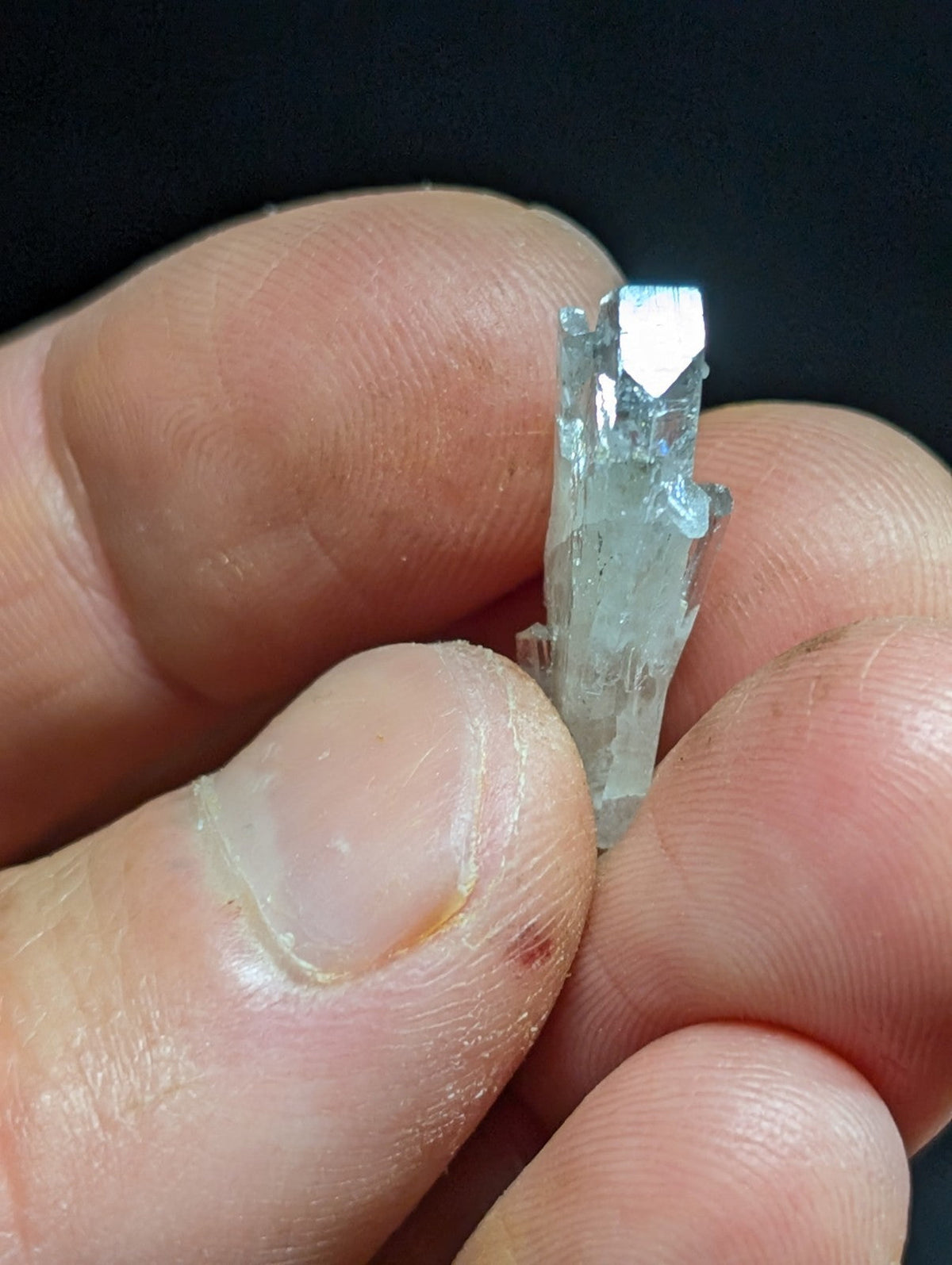 A translucent, pale blue crystal with a faceted top and rougher base is held between fingers.