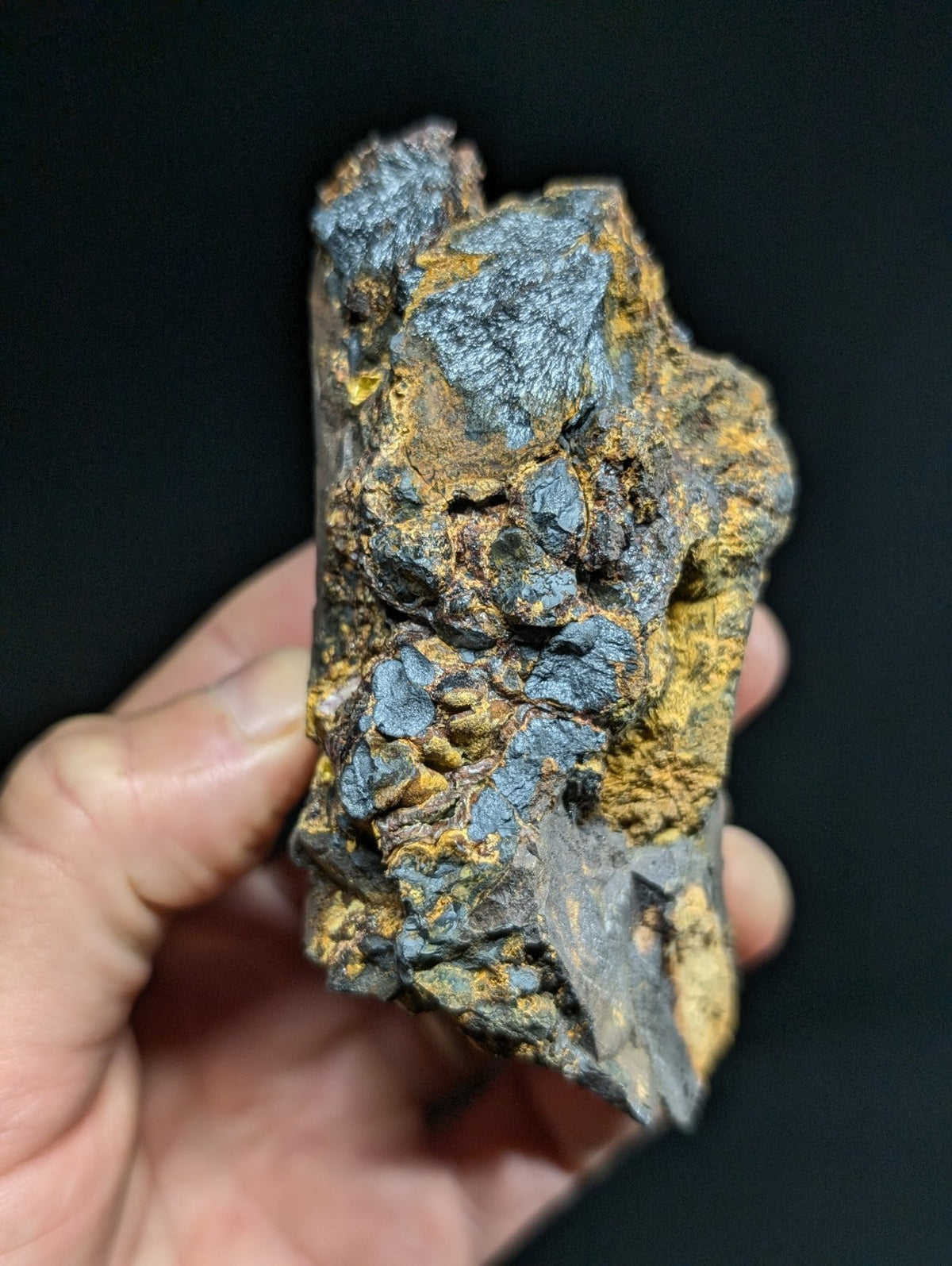 A rugged, irregularly shaped mineral specimen with a striking contrast of deep blue-gray and vibrant yellow-orange patches.