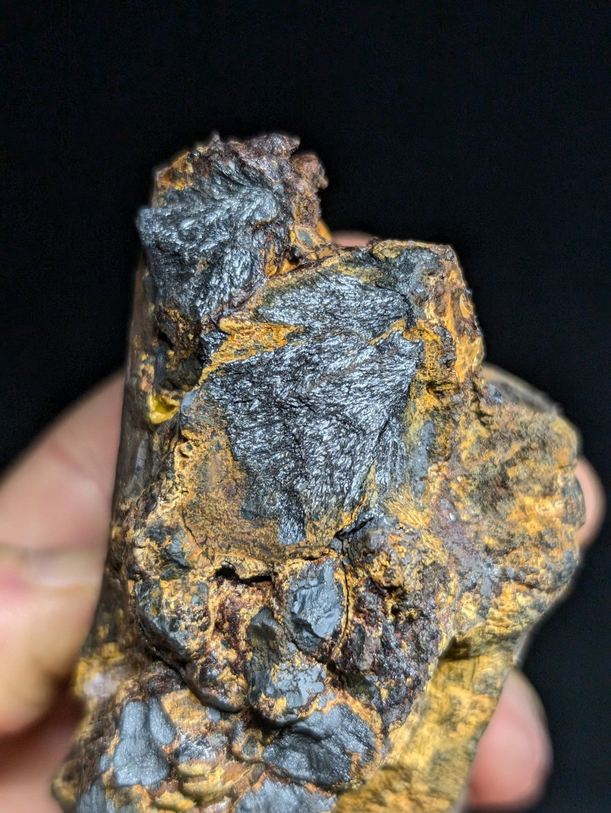 A rugged, irregularly shaped piece of ore with a dark metallic sheen and patches of vibrant yellow-orange mineral coating.