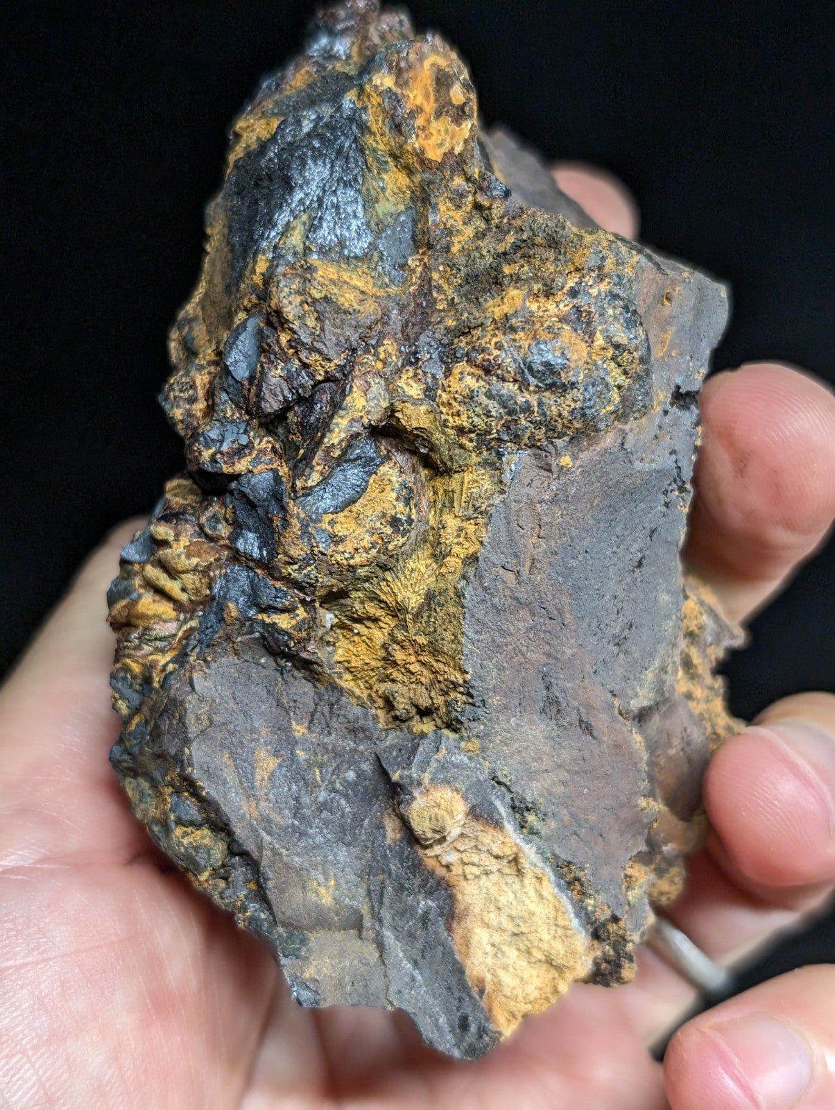 A rugged, irregularly shaped rock with a dark gray base and patches of vibrant orange-yellow mineral deposits.