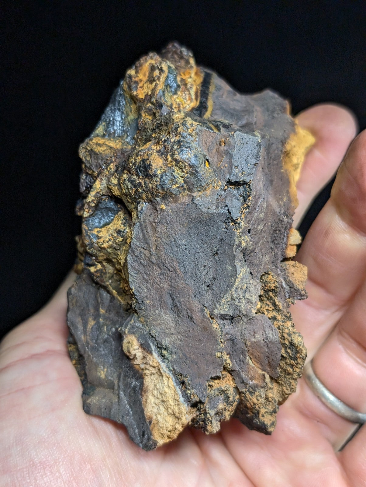 A rugged, irregularly shaped meteorite with a dark metallic core and patches of orange-yellow oxidation.