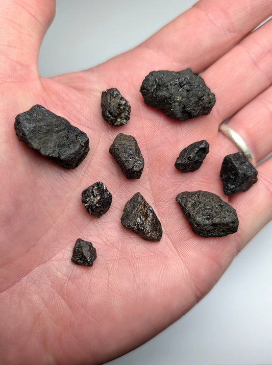 A collection of dark rough-textured titanium-bearing garnet meteorite fragments from magnet cove arkansas in an open palm