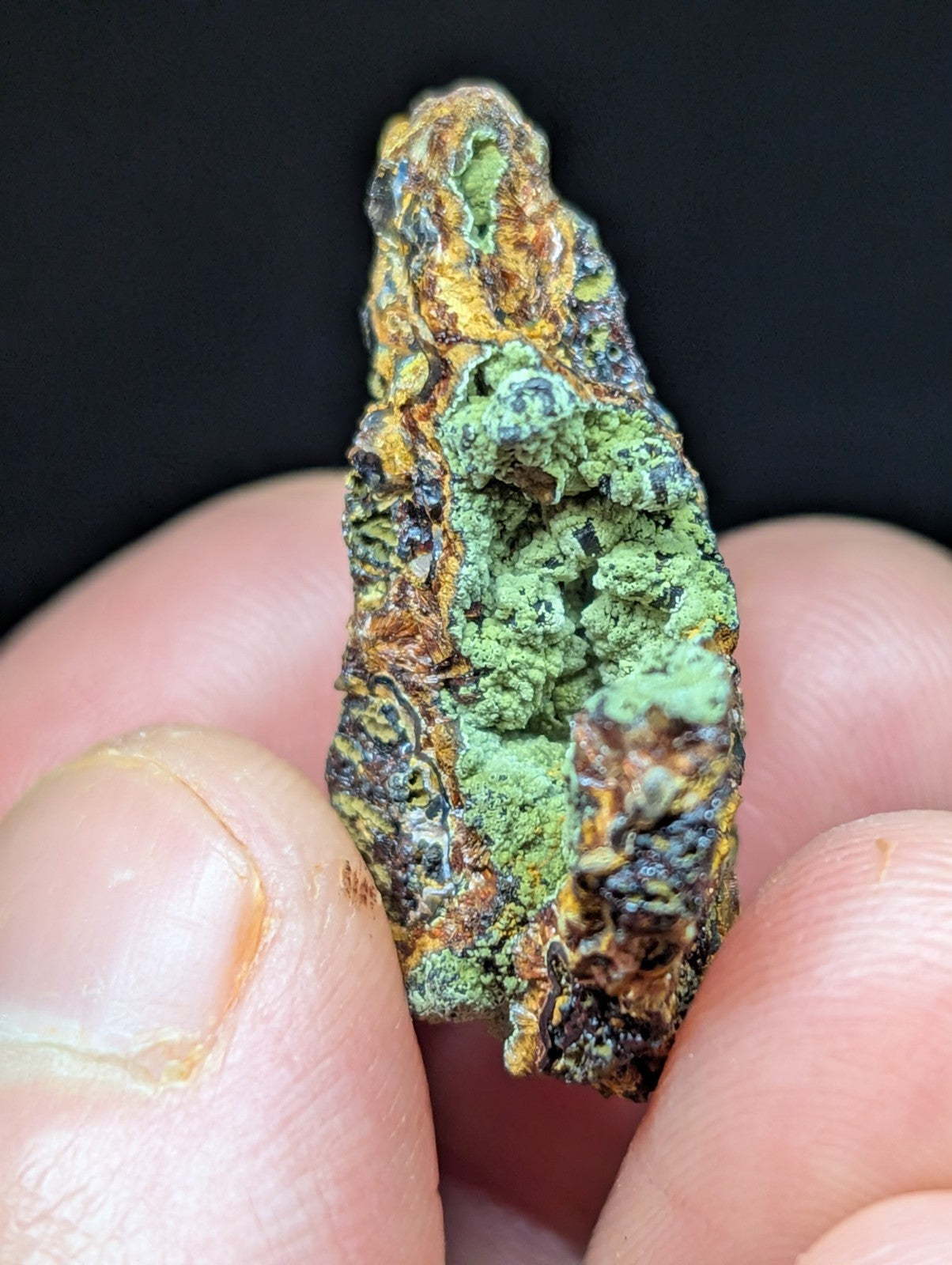 A rugged, irregularly shaped mineral specimen with patches of vibrant green moss-like growth over a base of rust-colored and darkened rock.