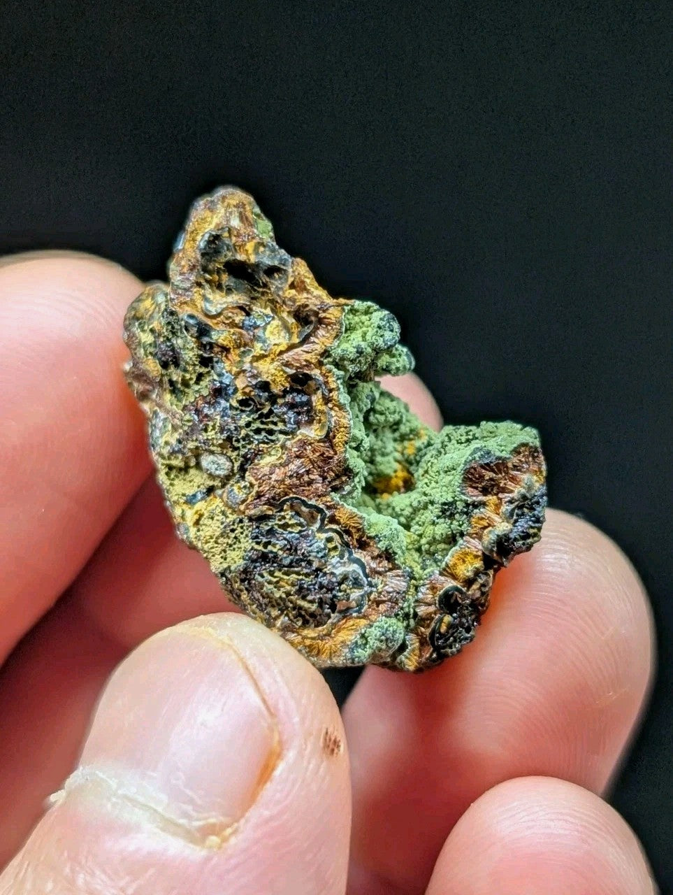 A rugged, irregularly shaped mineral specimen with a textured surface displaying patches of vibrant green, earthy brown, and darkened areas.