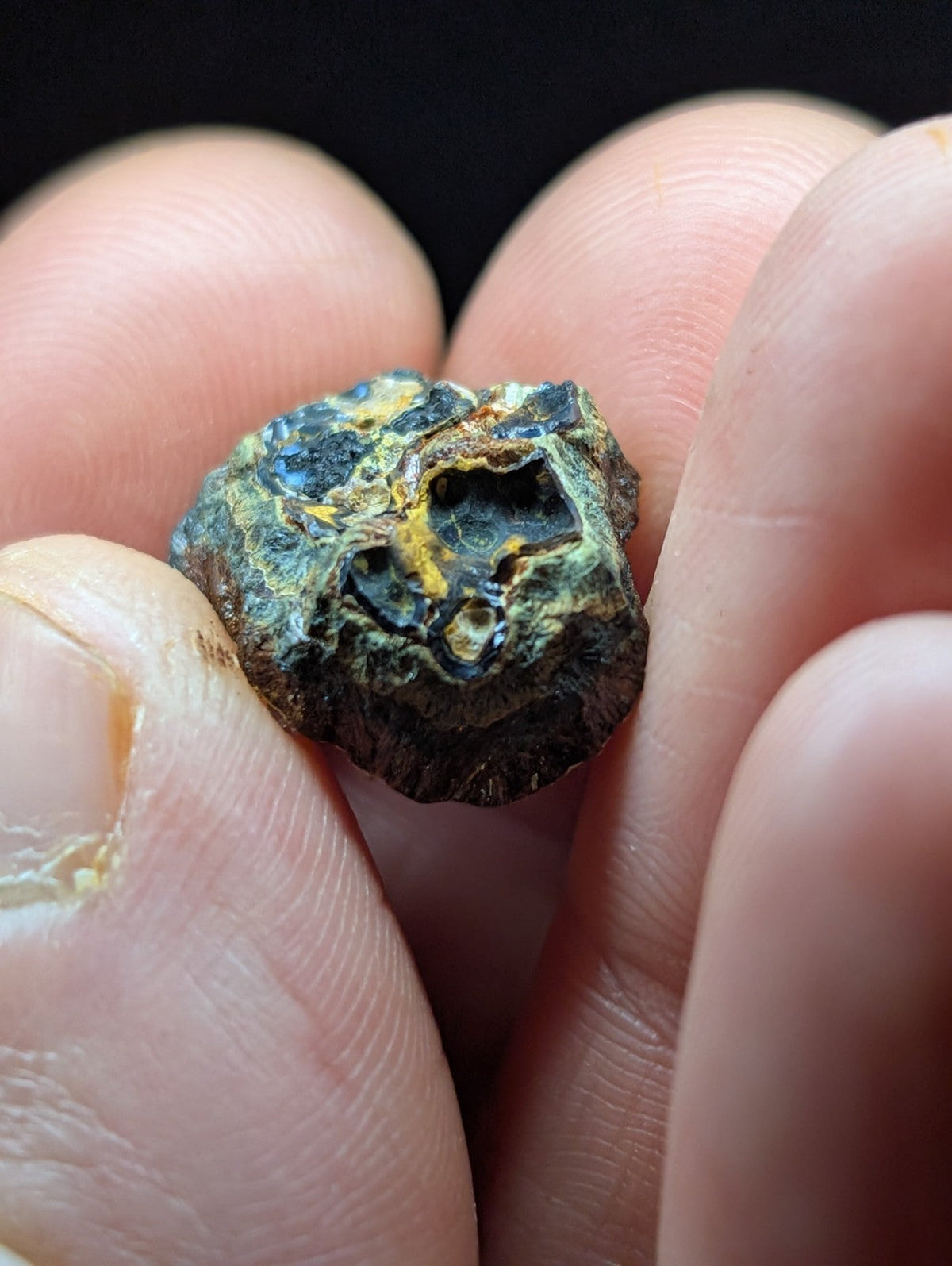 A rough, irregularly shaped mineral specimen with a mottled surface of dark green and yellowish hues.