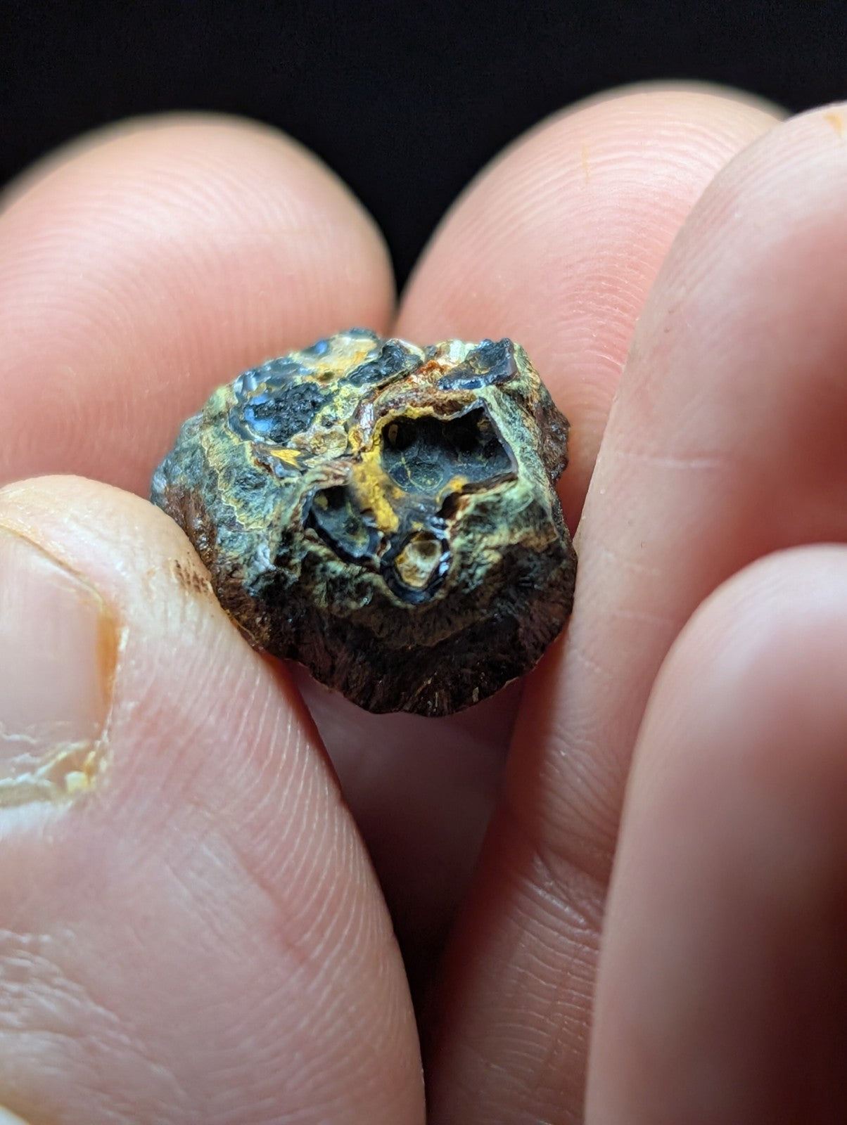 A rough, irregularly shaped mineral specimen with a mottled surface of dark green and yellowish hues.