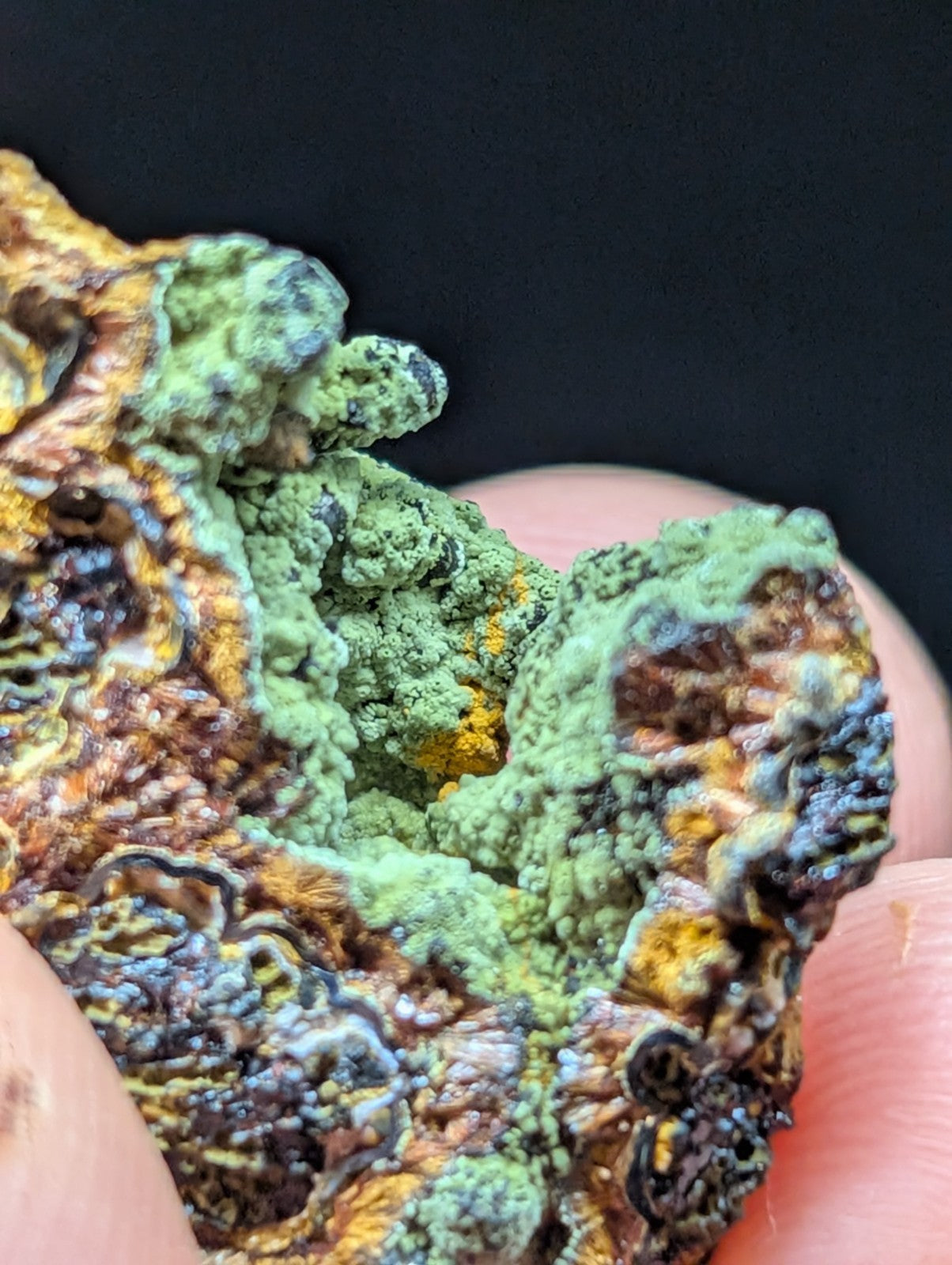 A textured, multicolored mineral specimen with vibrant green, orange, and brown hues.