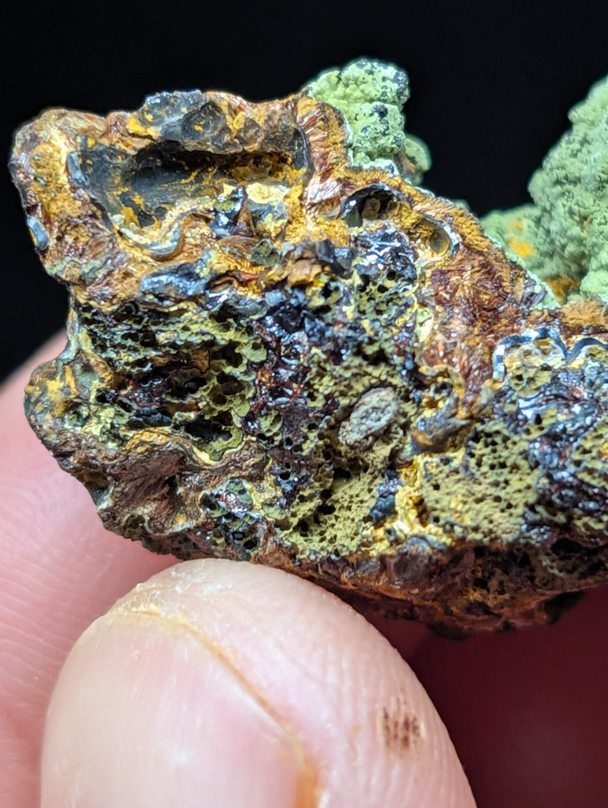 A rugged, irregularly shaped mineral specimen featuring a textured surface with patches of vibrant green, earthy brown, and metallic gold hues.