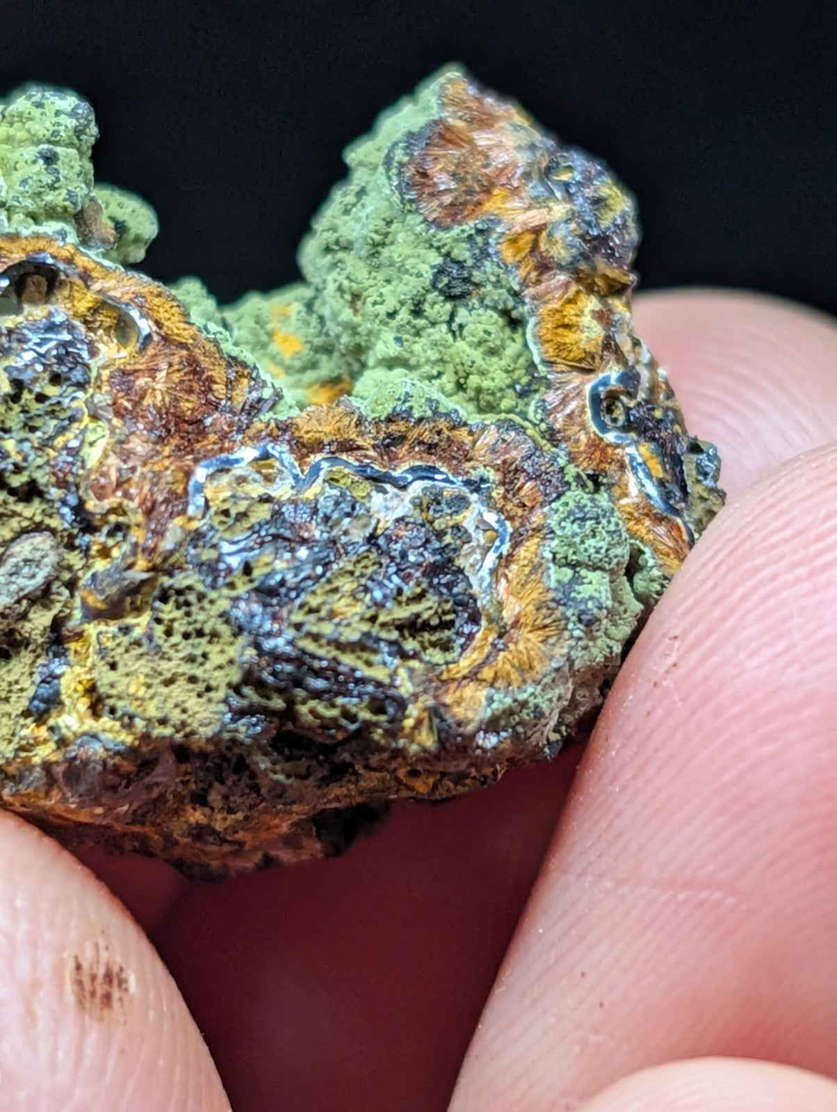 A rugged, irregularly shaped mineral specimen with vibrant green and orange-brown patches, accented by metallic blue streaks.