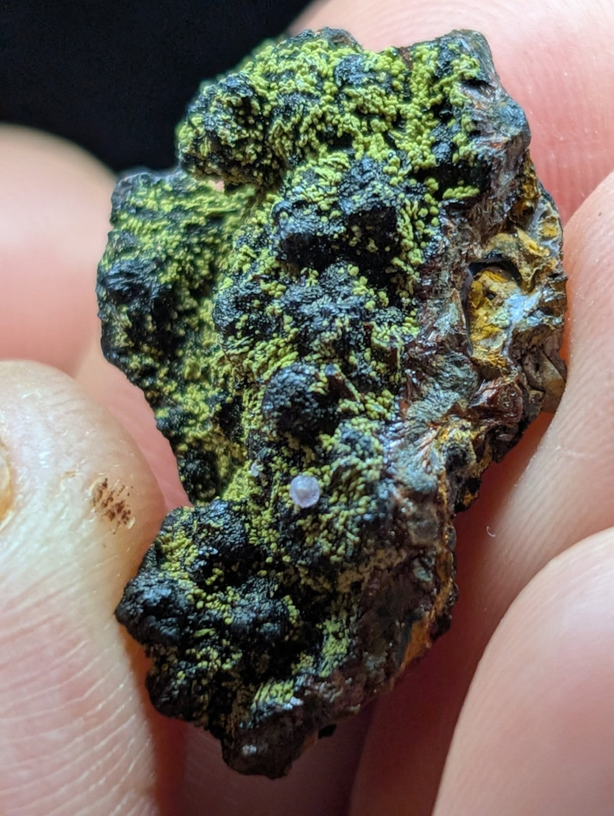 A rough, irregularly shaped mineral specimen with vibrant green moss-like patches covering a dark, textured base.