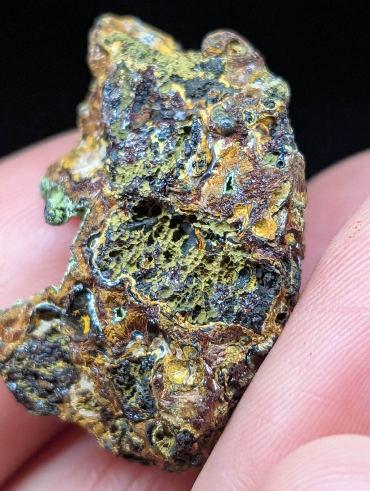 A rugged, irregularly shaped mineral specimen with a textured surface displaying patches of greenish-yellow and dark brown hues.